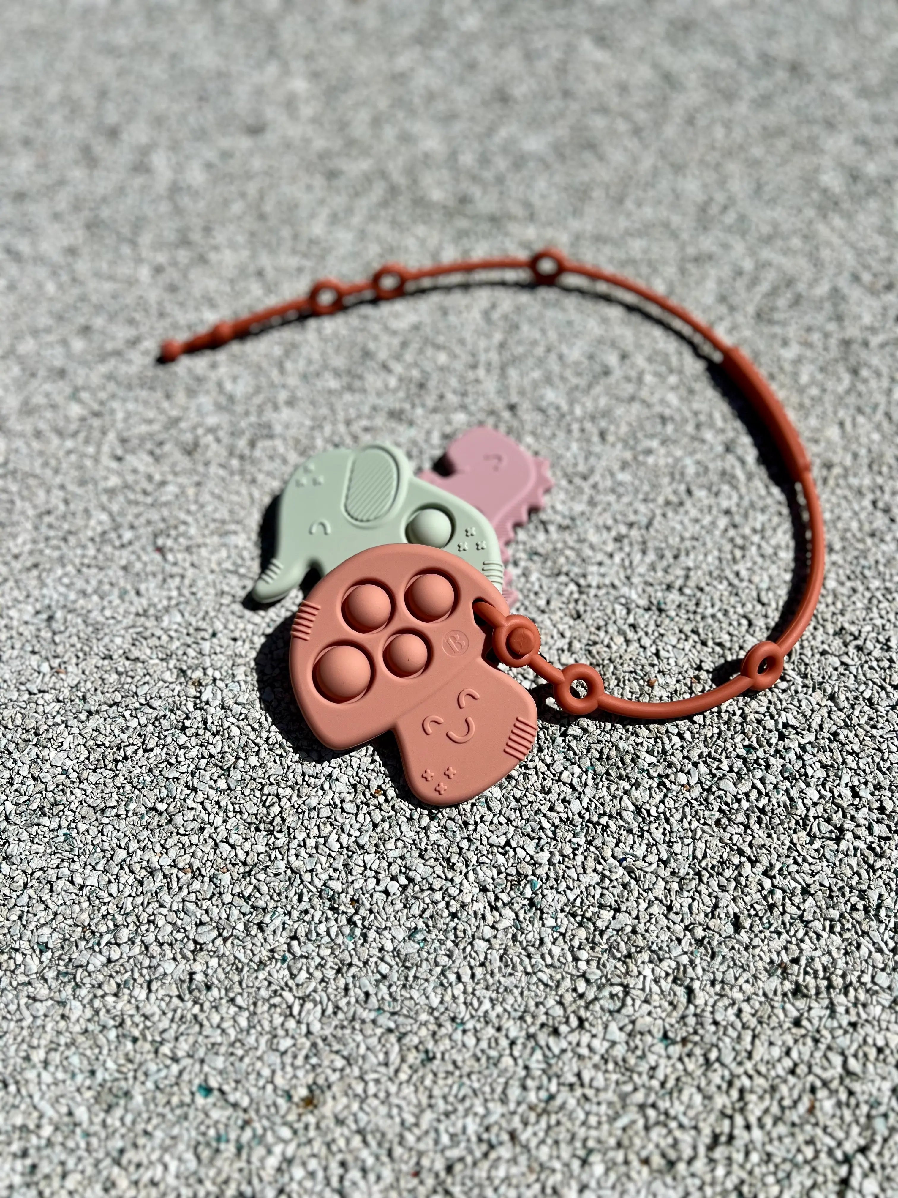 Anneau de dentition Pop-It attaché à un attache doudou Lovie Link® de Bim Bam Bloom, permettant à bébé de mâcher en toute sécurité lors de ses aventures.