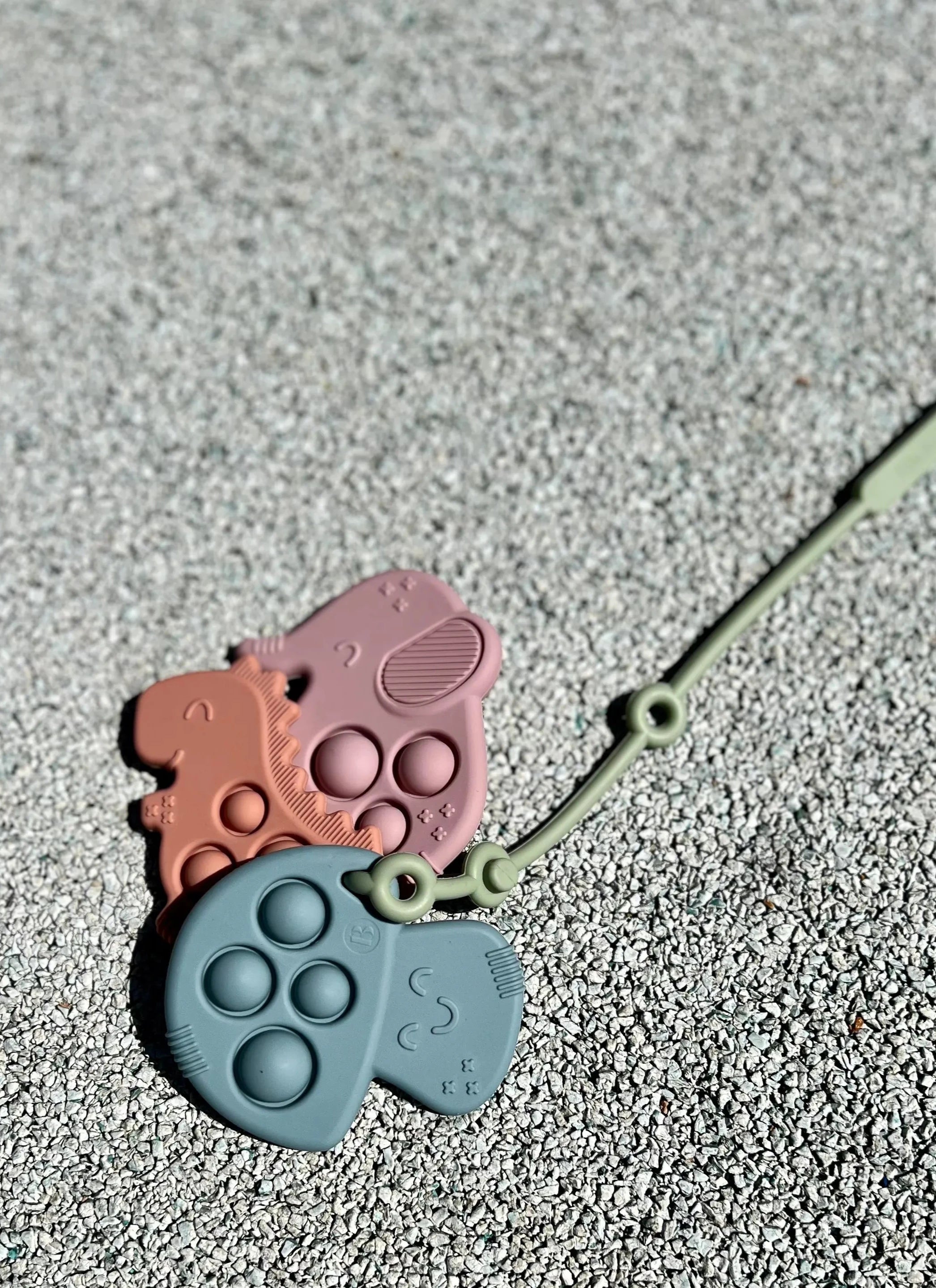 Anneau de dentition Pop-It attaché à un Lovie Link® de Bim Bam Bloom, permettant à bébé de mâcher en toute sécurité lors de ses aventures.