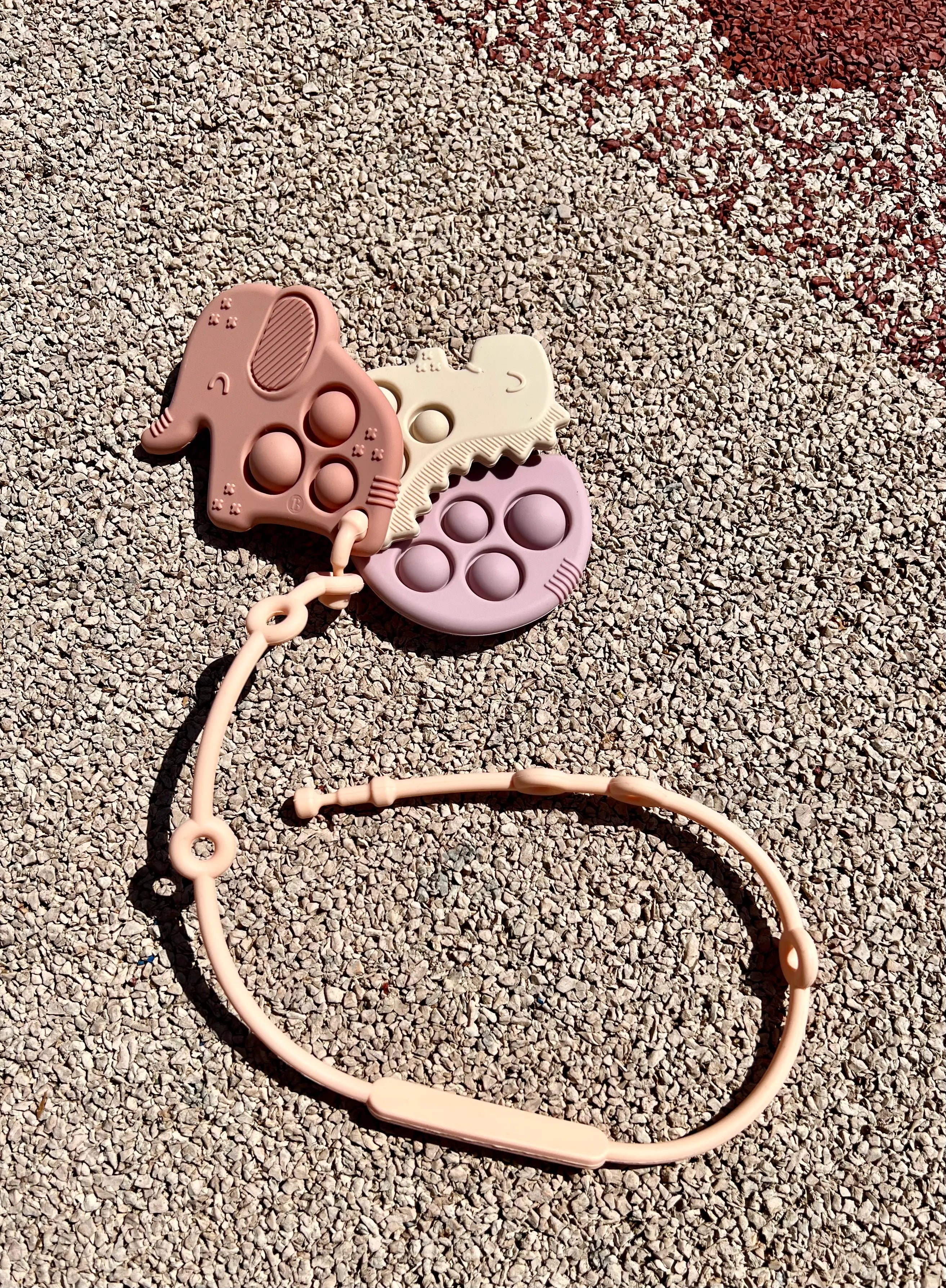 Anneau de dentition Pop-It attaché à un attache doudou Lovie Link® de Bim Bam Bloom, permettant à bébé de mâcher en toute sécurité lors de ses aventures.