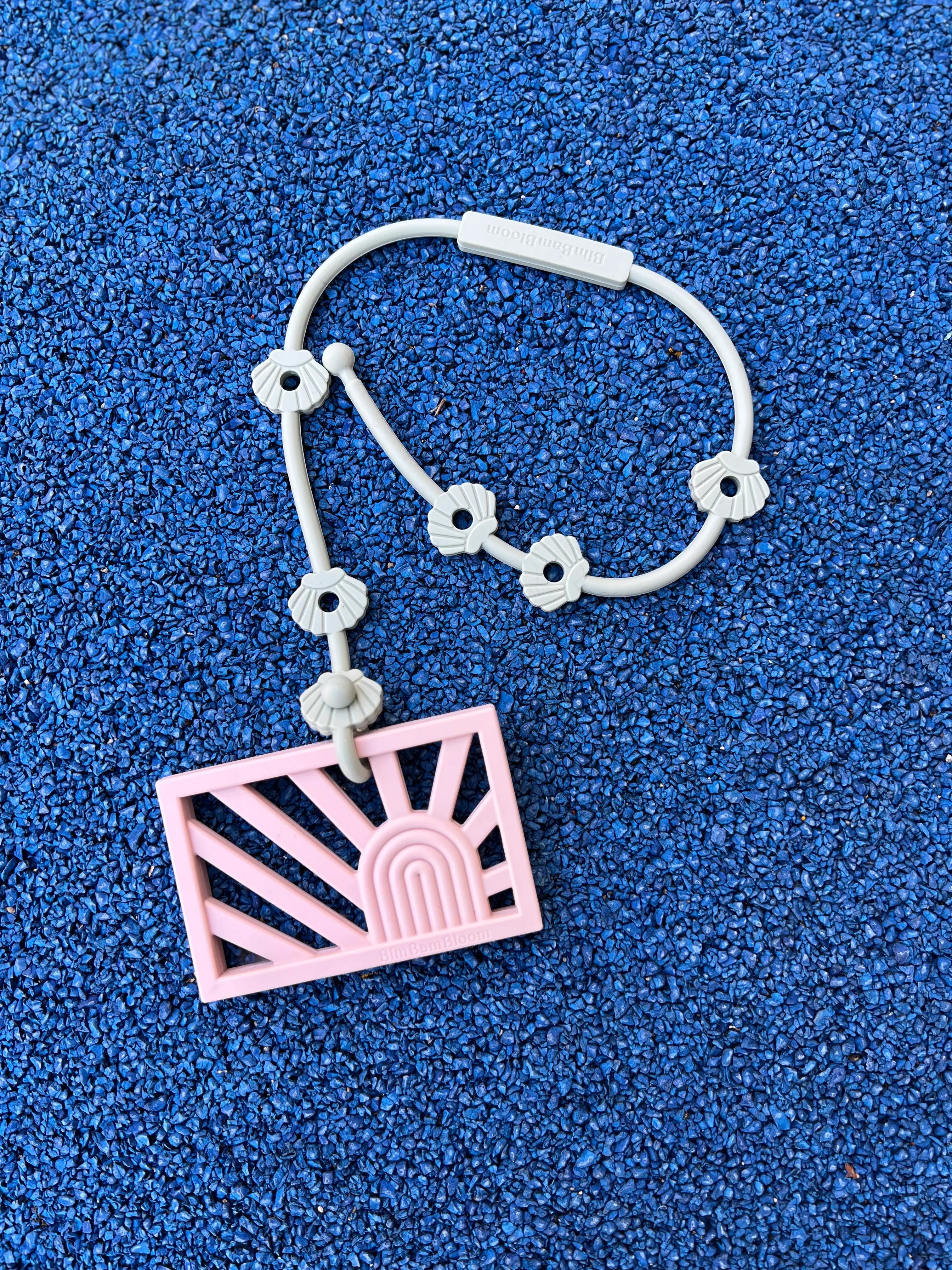 Anneau de dentition Rainbow Rose Pétale attaché à un attache-doudou Lovie Link® pour mâchouiller en toute tranquillité, garantissant que le jouet reste toujours à portée de main par Bim Bam Bloom.