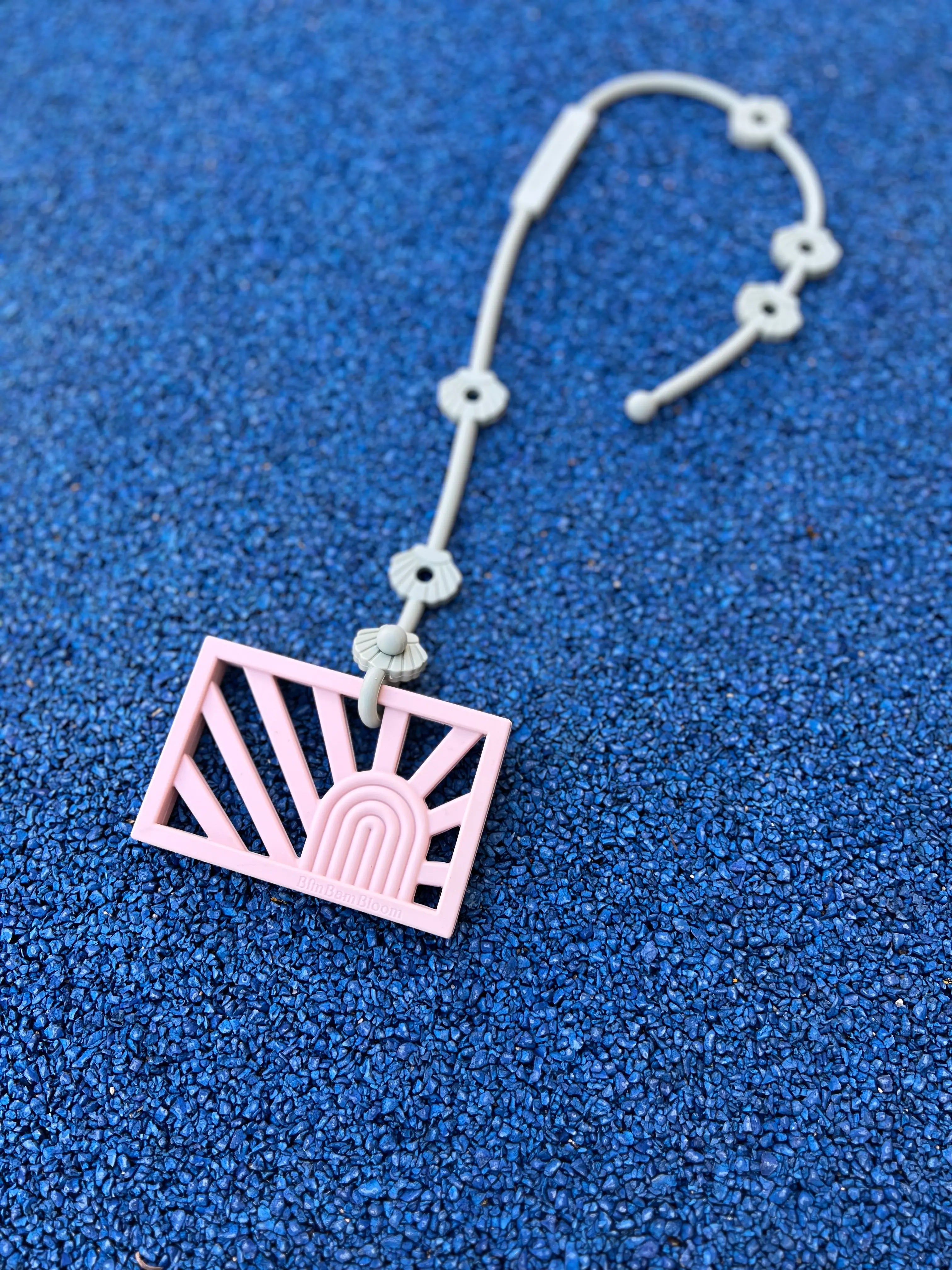 Anneau de dentition Rainbow Rose Pétale attaché à un attache-doudou Lovie Link® pour mâchouiller en toute tranquillité, garantissant que le jouet reste toujours à portée de main par Bim Bam Bloom.