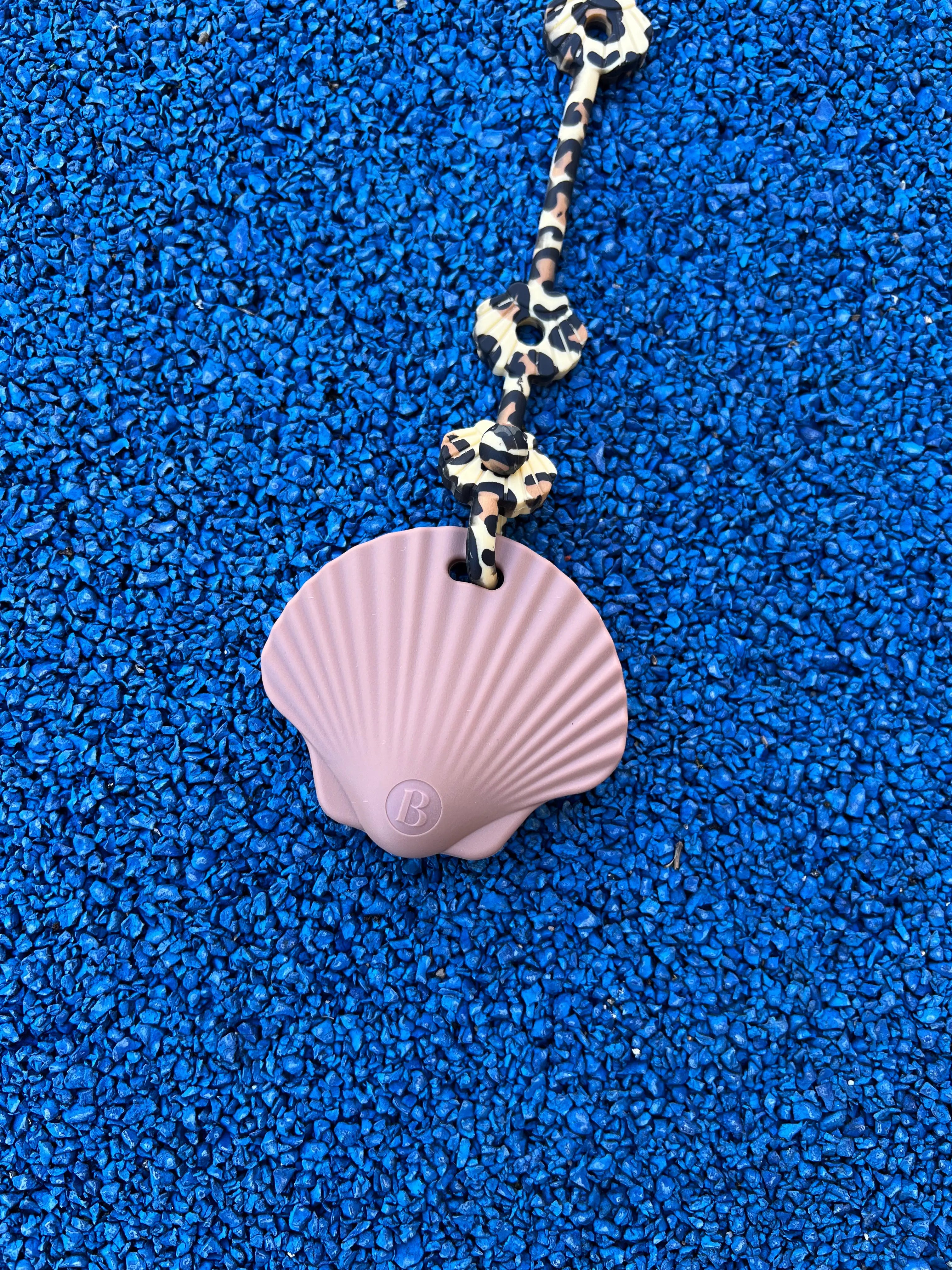 Gros plan sur anneau de dentition Shell Rose attaché à un attache doudou Lovie Link léopard, offrant sécurité et praticité lors des sorties par Bim Bam Bloom.