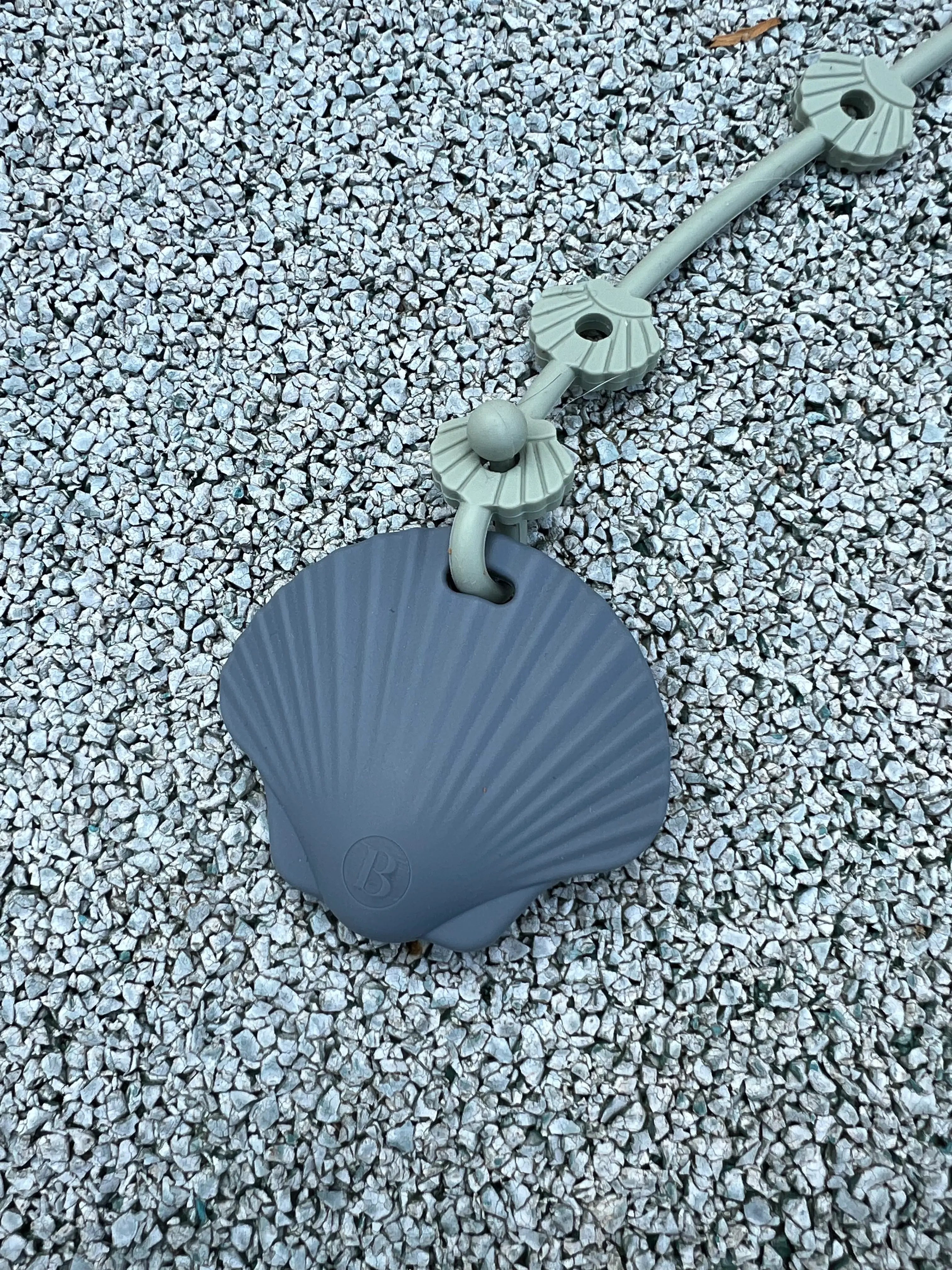 Anneau de dentition Shell Coquillage Gris attaché à un attache doudou Lovie Link Shell, offrant sécurité et praticité lors des sorties.