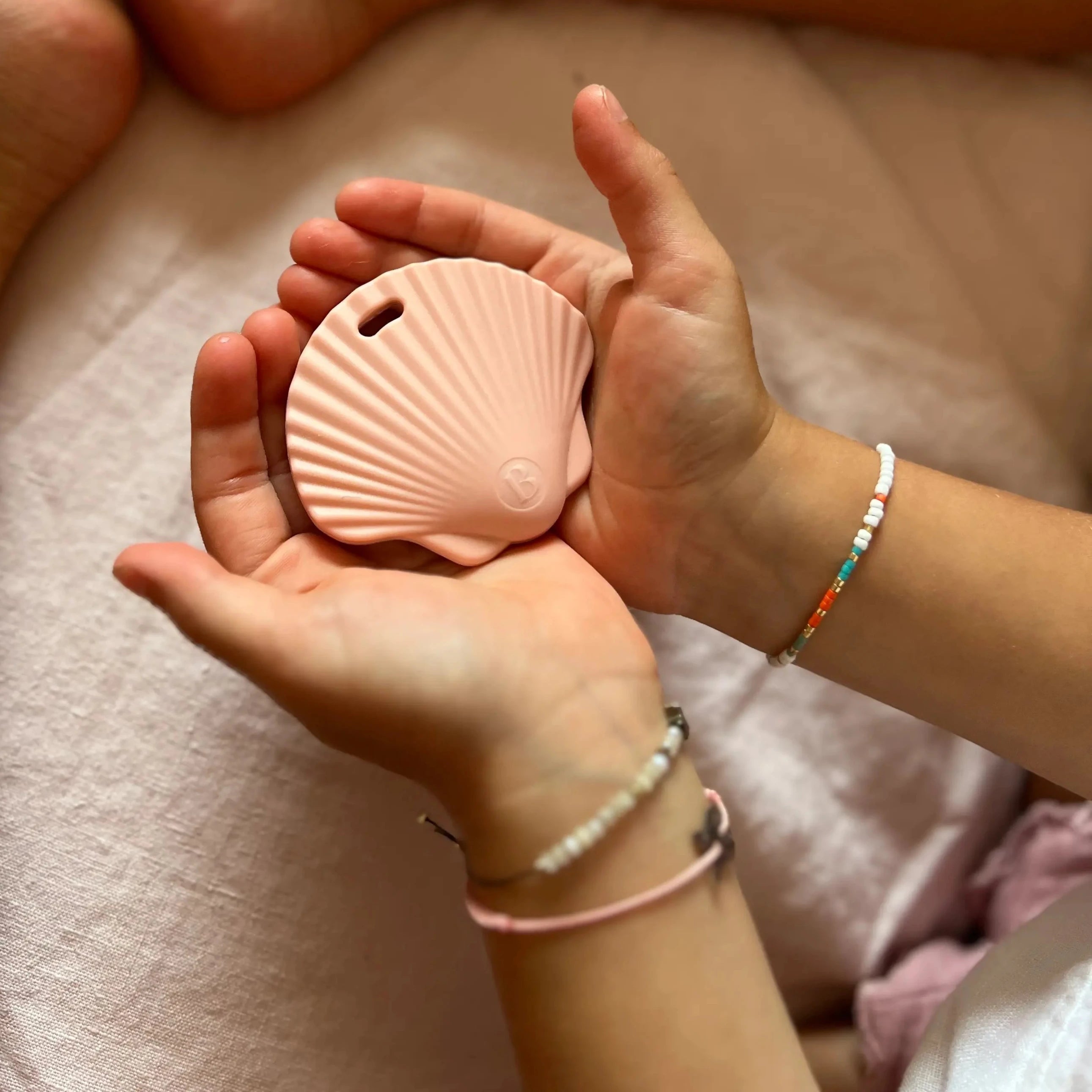 Petite fille tenant l'anneau de dentition Shell Rose Guimauve Fondante, un accessoire doux et réconfortant pour soulager les gencives de baby.