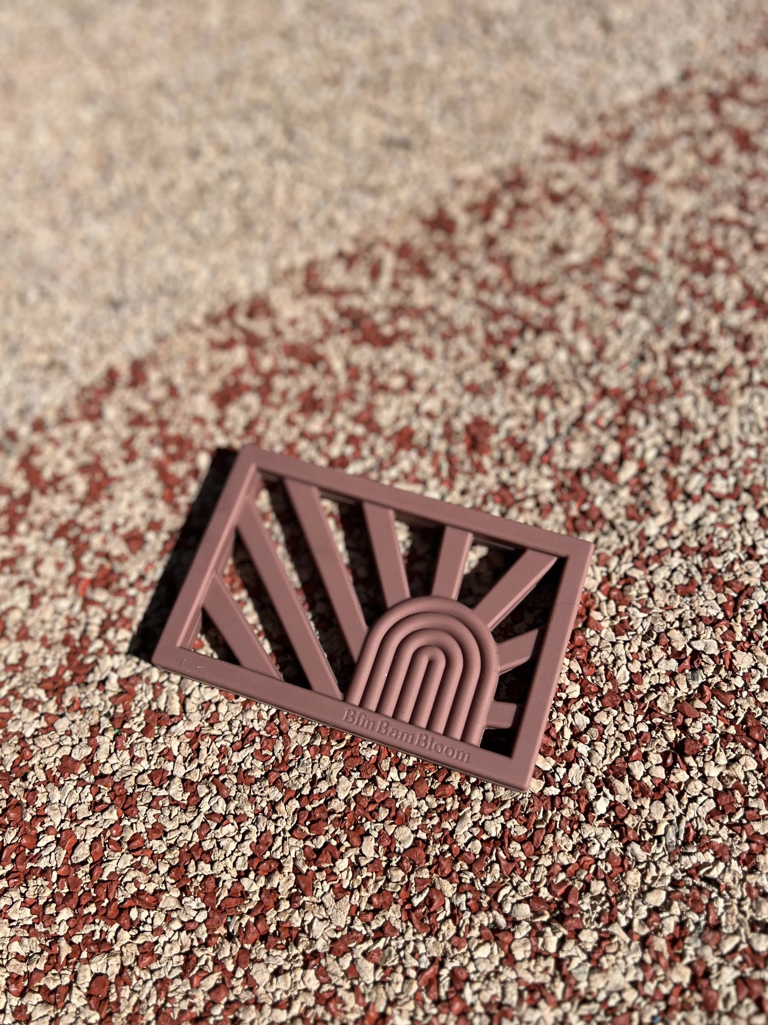 Anneau de dentition Rainbow en couleur Terracotta sur un fond pastel, un jouet de dentition au design arc-en-ciel sûr et sain pour apaiser les gencives de bébé.