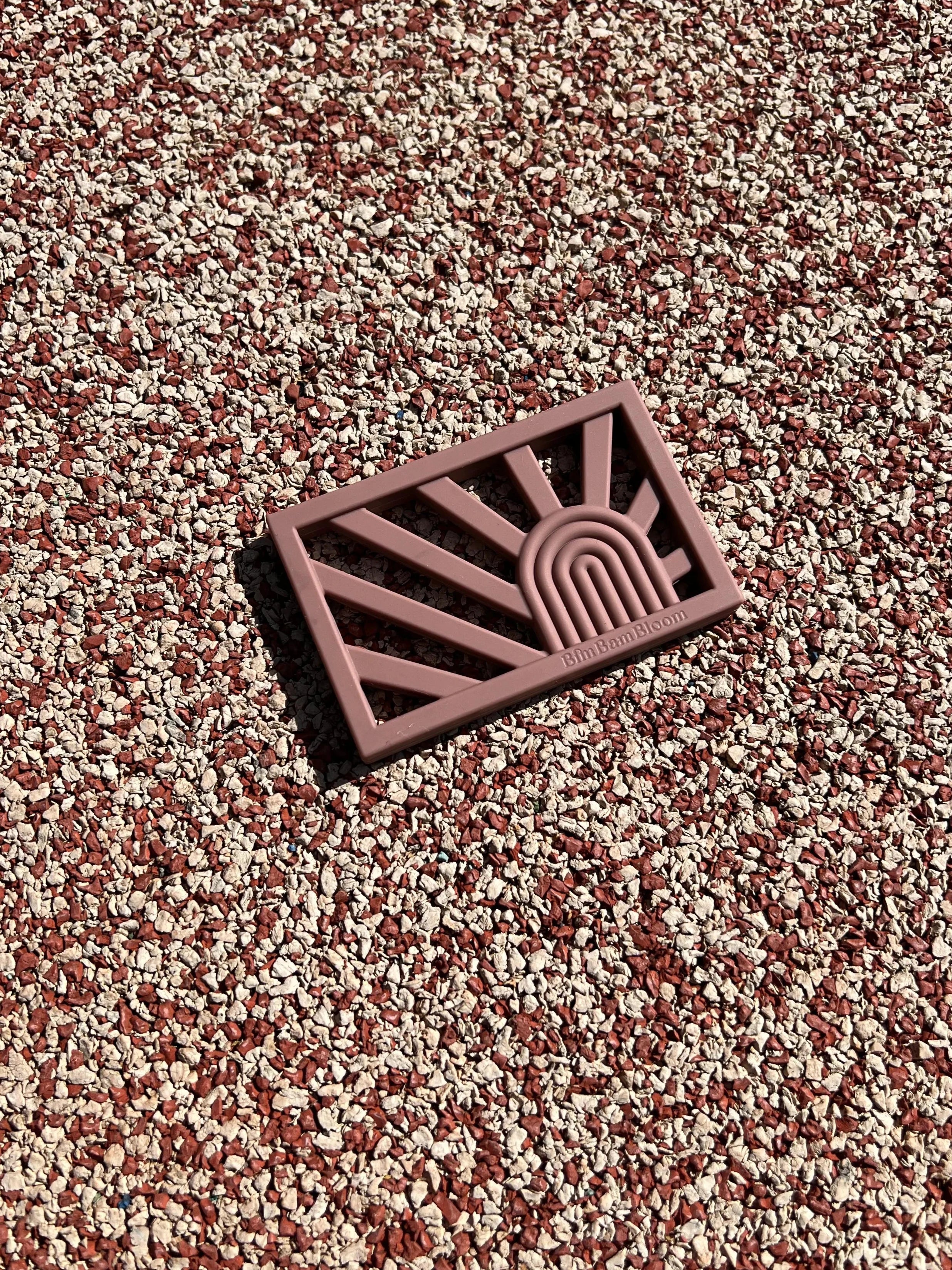 Anneau de dentition Rainbow en couleur Terracotta sur un fond pastel, un jouet de dentition au design arc-en-ciel sûr et sain pour apaiser les gencives de bébé.
