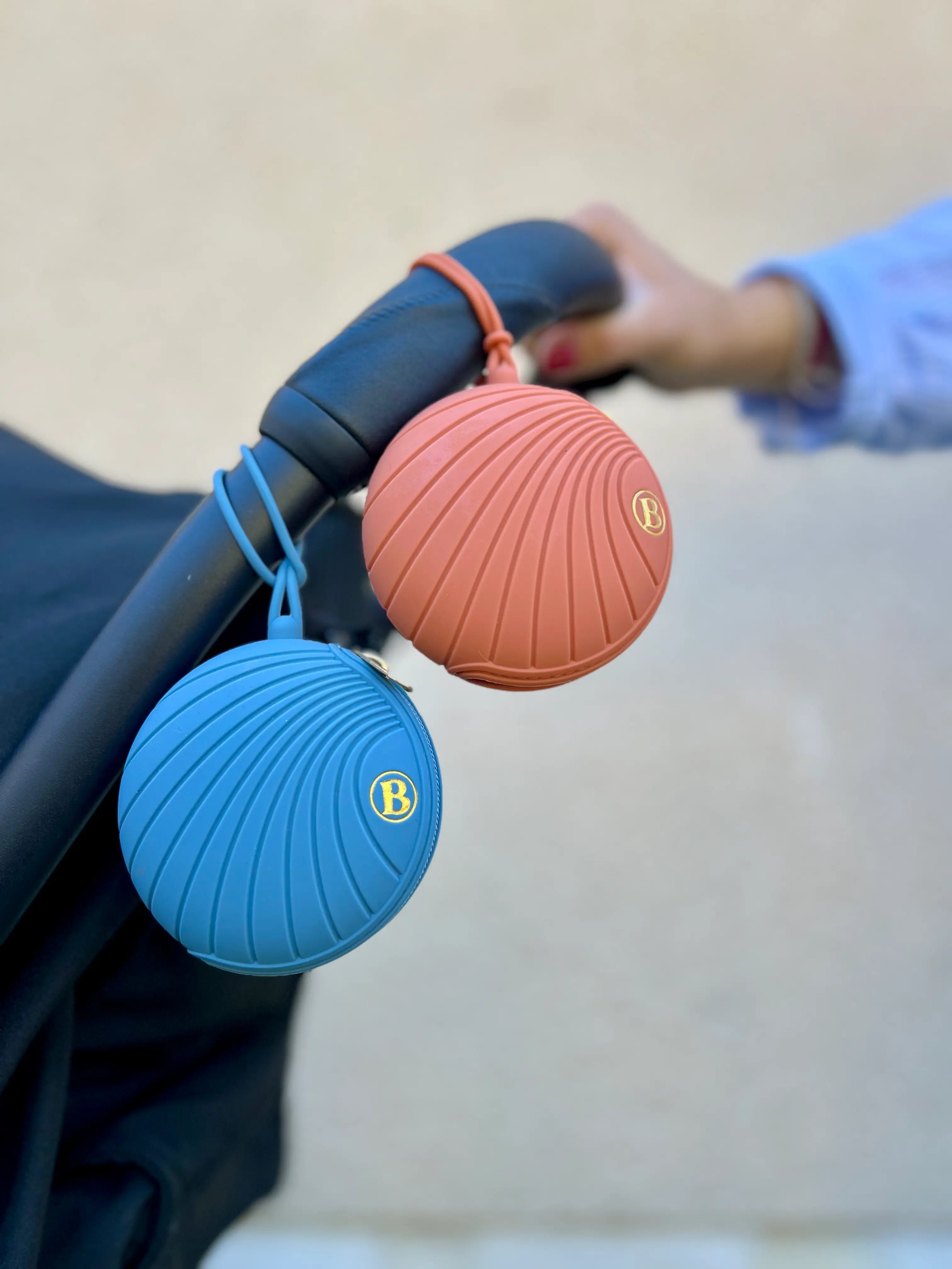 Deux boîtes à tétines accrochées à la poussette : une boîte à tétine bleue et une boîte à tétines terracotta Bim Bam Bloom