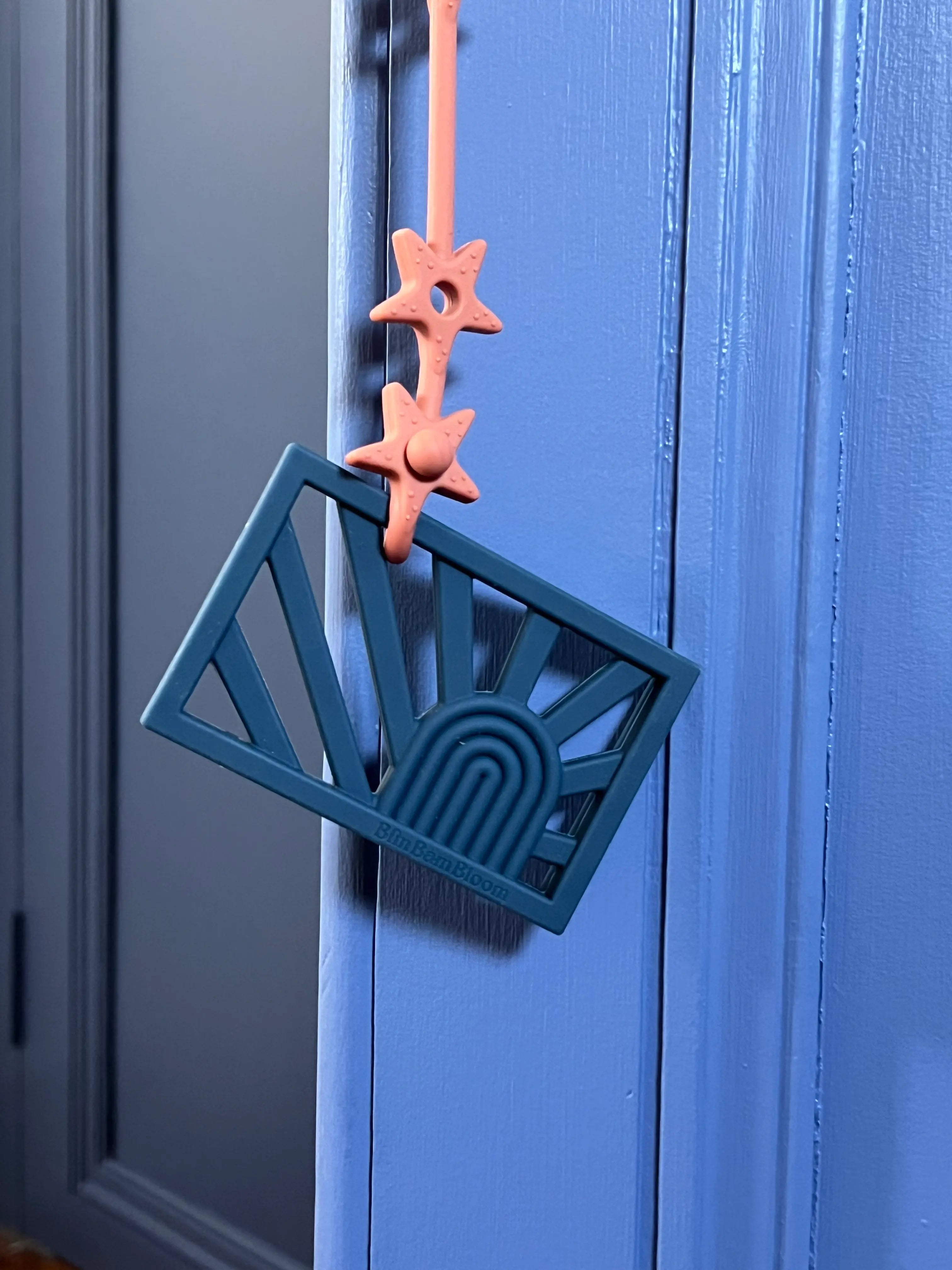 Anneau de dentition Rainbow Bleu attaché à un attache-doudou Lovie Link® Star pour mâchouiller en toute tranquillité, garantissant que le jouet de dentition reste toujours à portée de main.