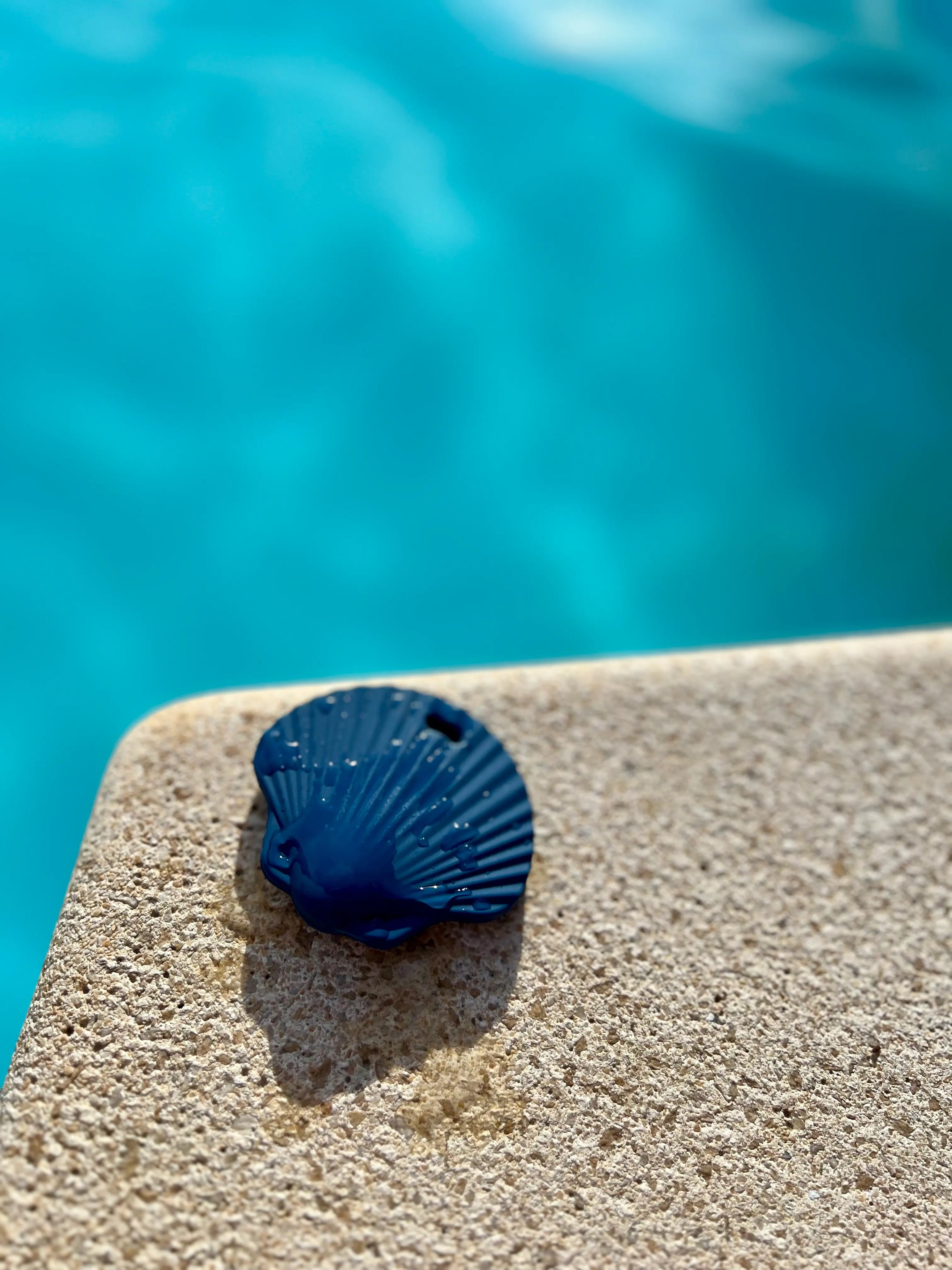 Anneau de dentition Shell coquillage en bleu celeste au bord d'une piscine. Fabriqué en silicone 100% sain pour apaiser les gencives de bébé.