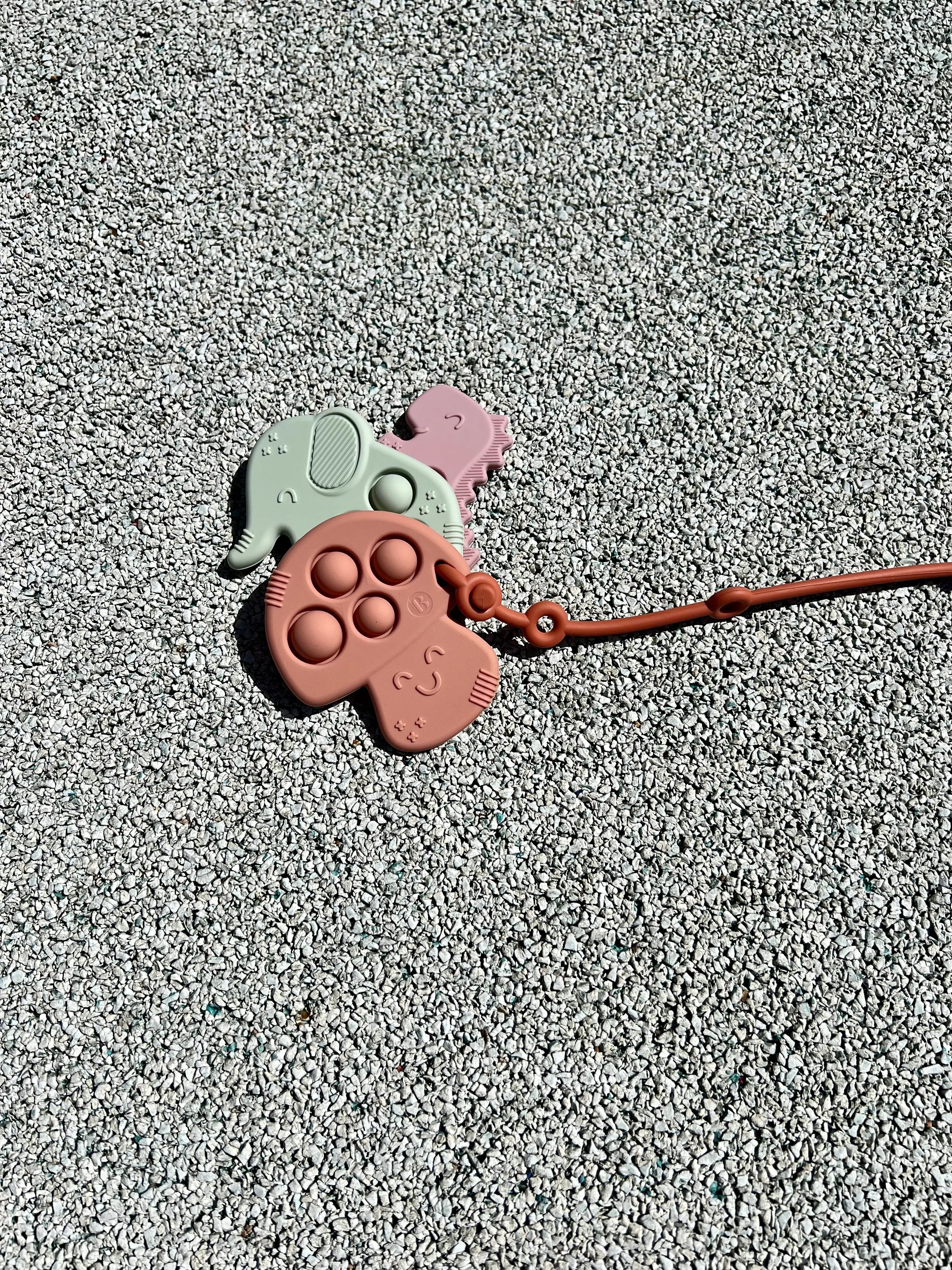 Attache doudou Lovie Link Terracotta attaché à nos anneaux de dentition Pop-it Bim Bam Bloom qui se fixe facilement à la poussette de votre bébé.