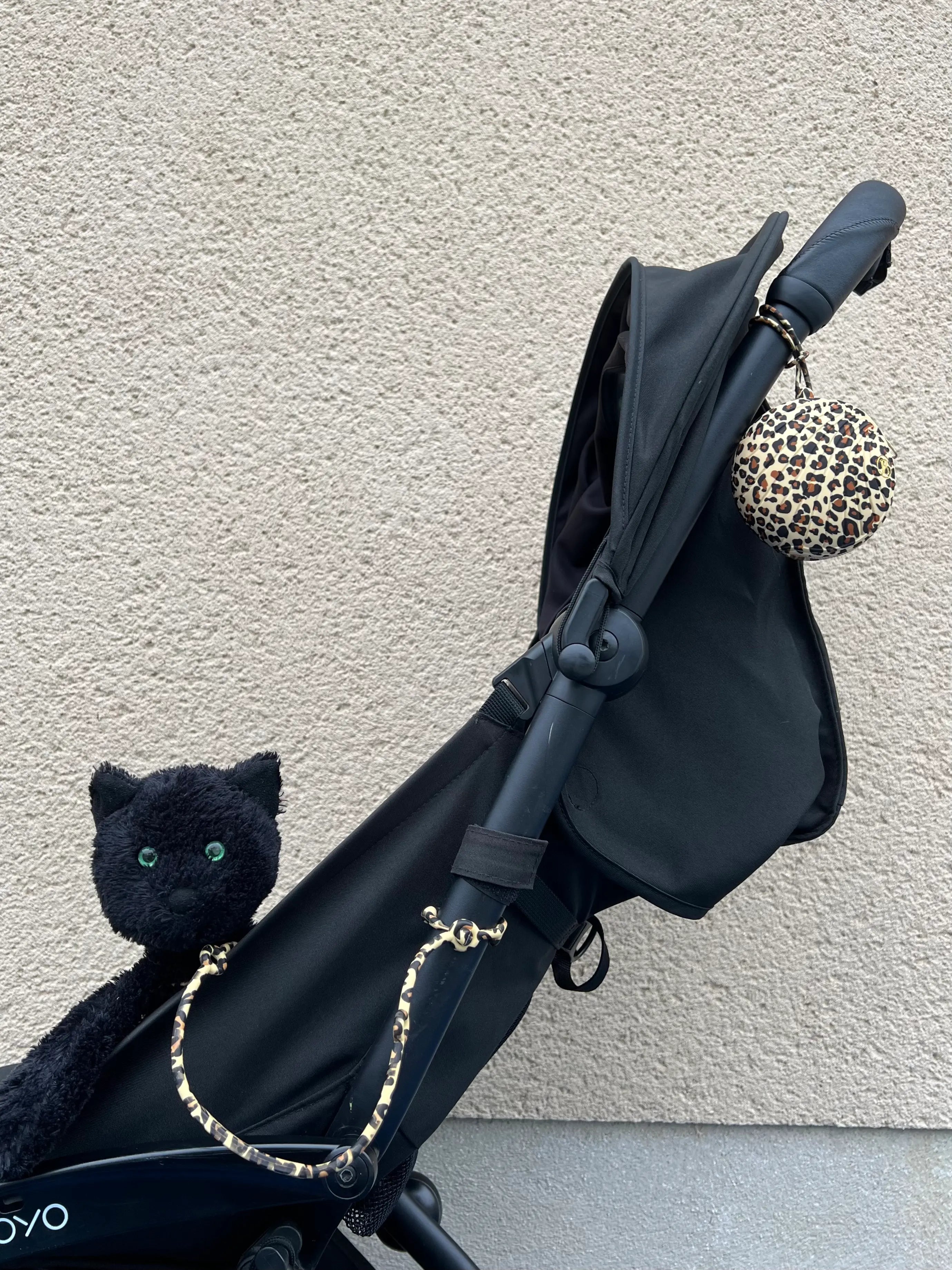 Notre adorable attache doudou Lovie Link Léopard accroché à une poussette noir et attaché à un doudou chat noir. Notre boite à tétine est attachée à la poussette. Nos laisses à doudou Lovie Link sont des accessoires indispensables pour les bébés et les parents !