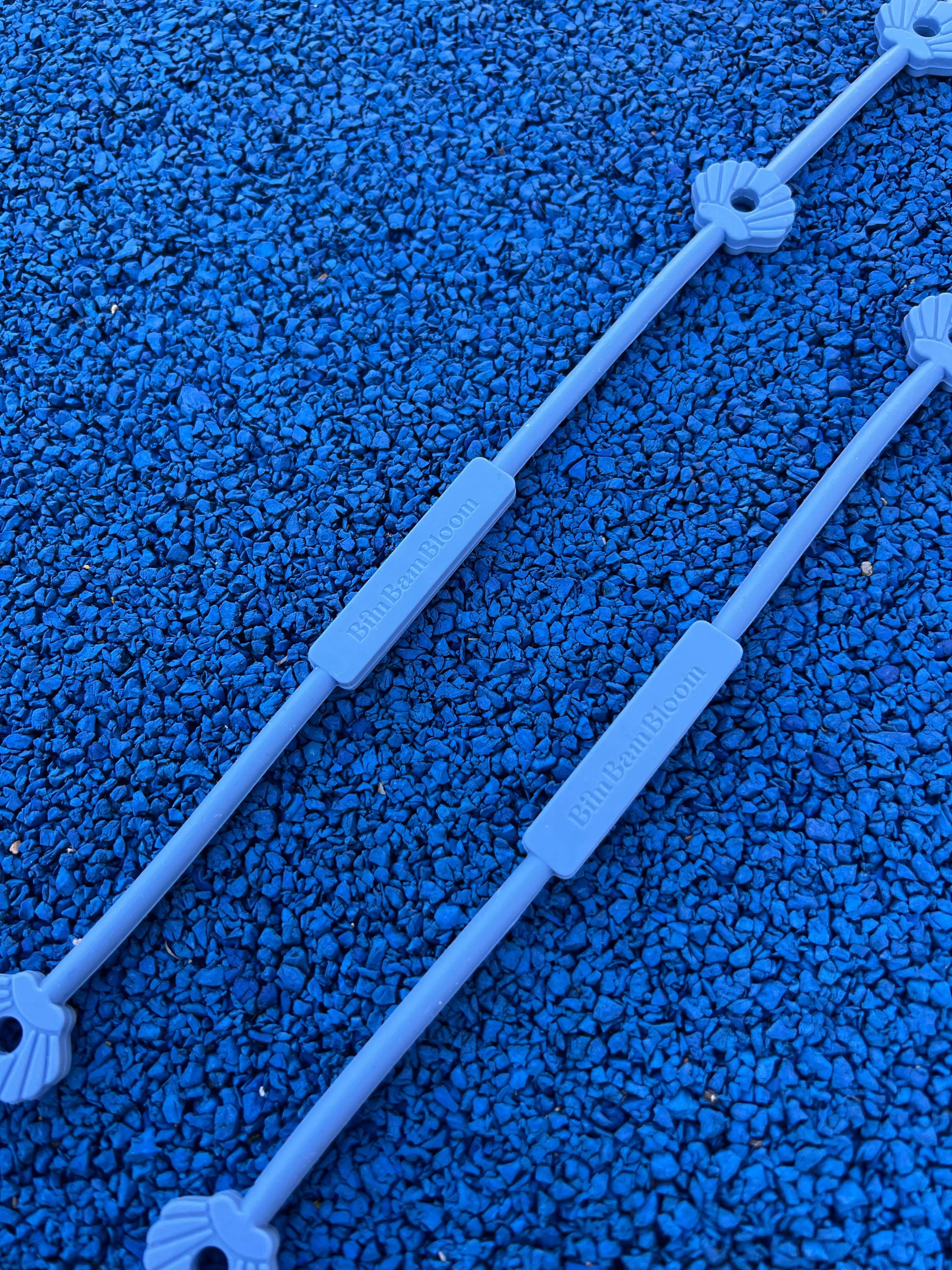 Gros plan sur le logo Bim Bam Bloom et les coquillages de nos attaches doudous pour poussette Lovie Link® Shell en bleu reve de farniente, un accessoire indispensable pour garder le doudou de bébé toujours à portée de main. Fini les doudous perdus !