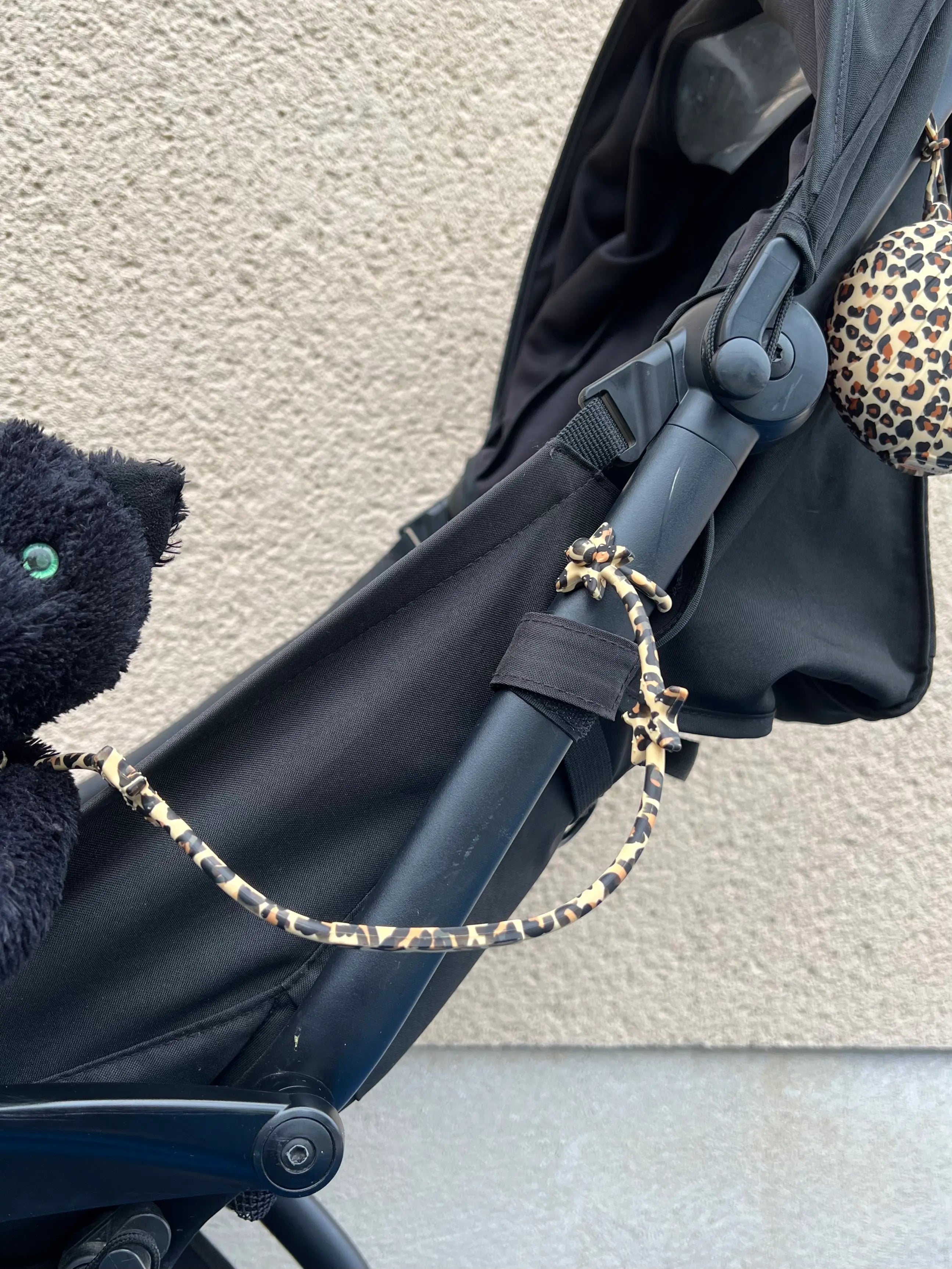 Gros plan sur la aisse à doudou Lovie Link® Star Léopard Bim Bam Bloom attachée à une poussette, garantissant des sorties stylées et organisées pour les parents.