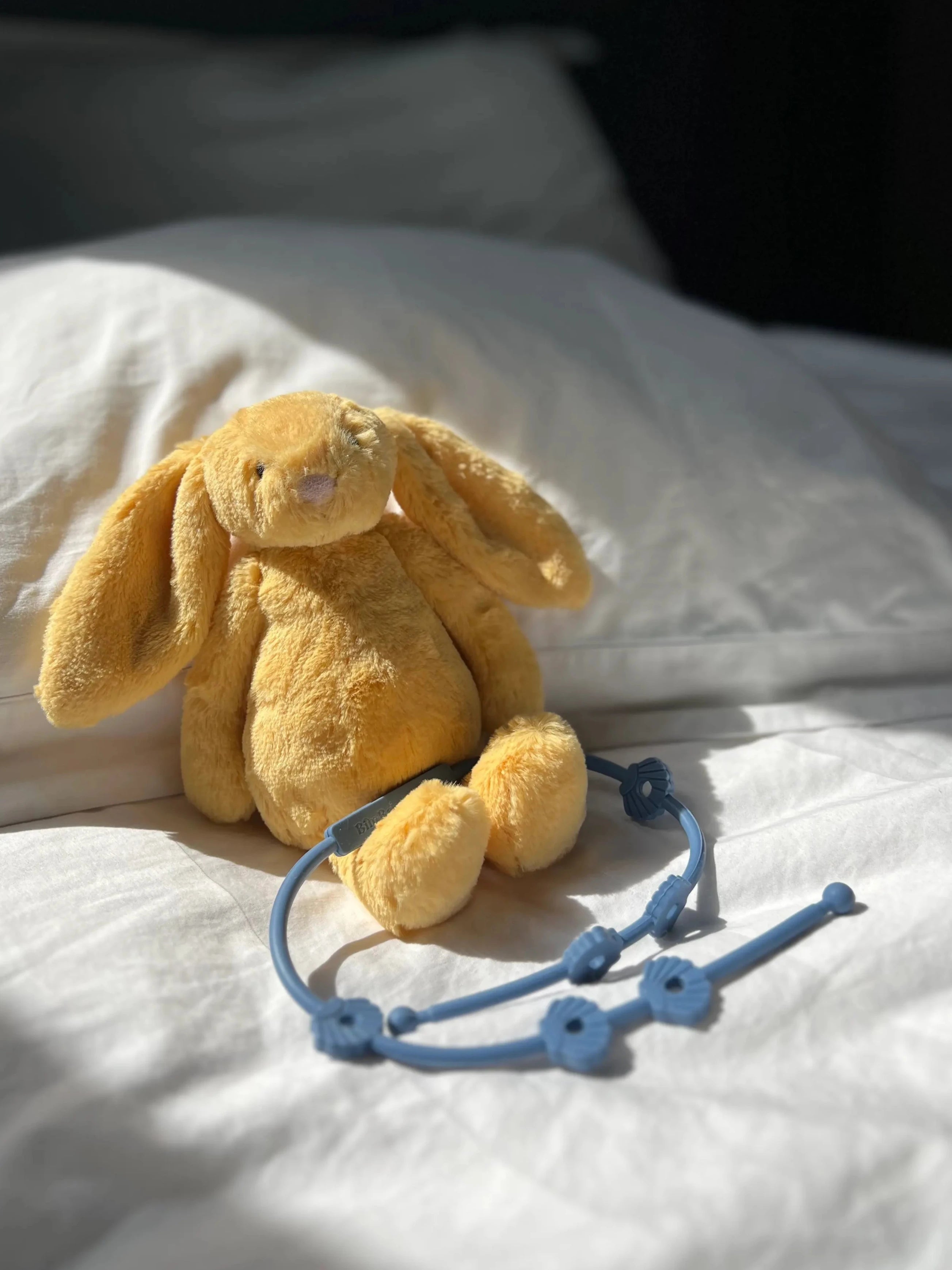 Laisse à doudou Lovie Link® Shell bleu reve de farniente attachée à un doudou lapin Bim Bam Bloom, pour des sorties sereines et organisées.