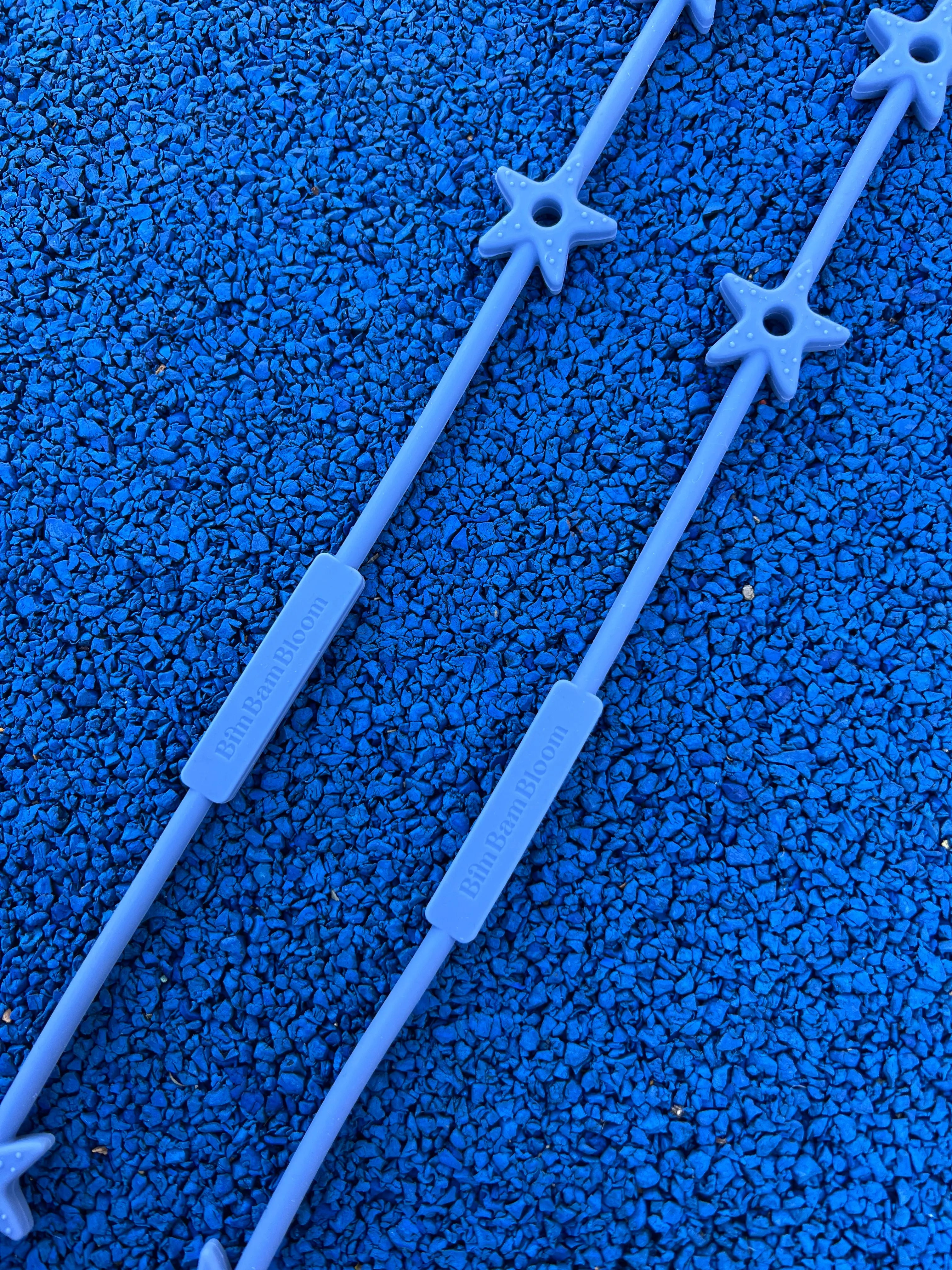 Gros plan sur le logo Bim Bam Bloom et les étoiles texturées de nos attaches doudou Lovie Link® Star en bleu reve de farniente. Accessoire indispenssable pour garder le doudou de bébé toujours à portée de main et en securité.