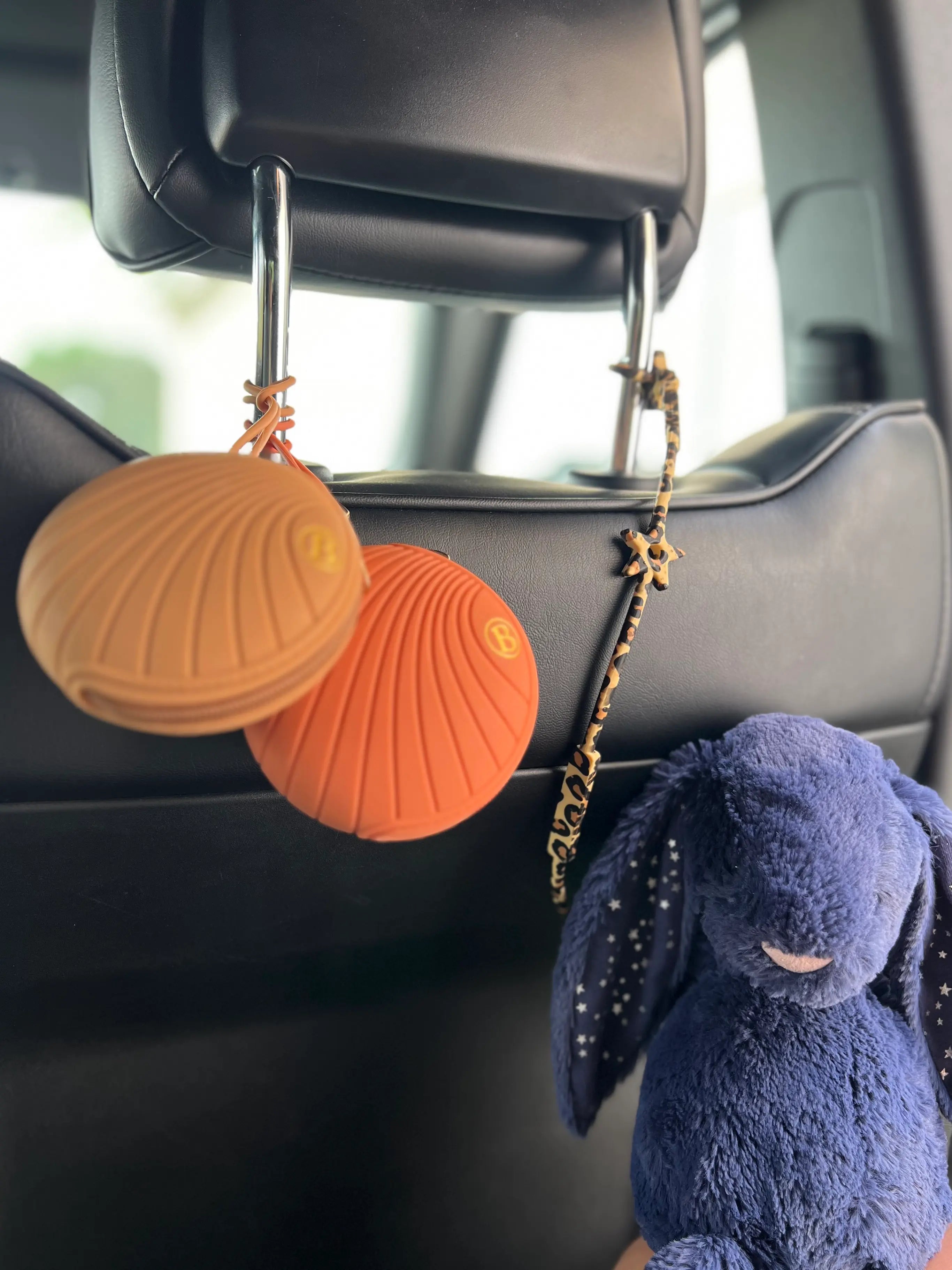 Lovie Link® Star Léopard accroché à l'appui-tête d'une voiture, avec deux boîtes à tétines également fixées, illustrant un voyage en toute sécurité et praticité pour bébé.