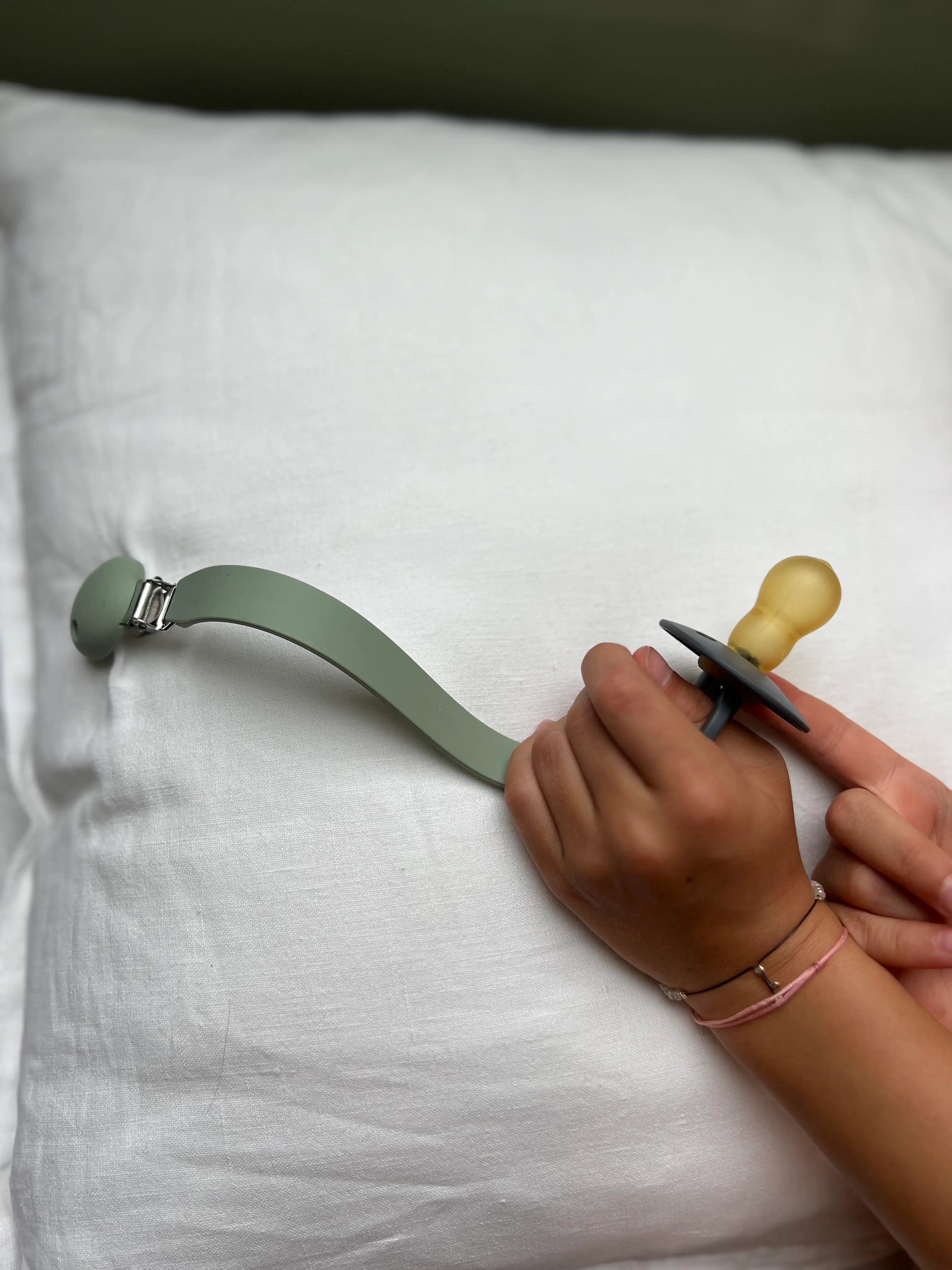 Attache tetine en silicone vert Bim Bam Bloom dans la main d'une petite fille.