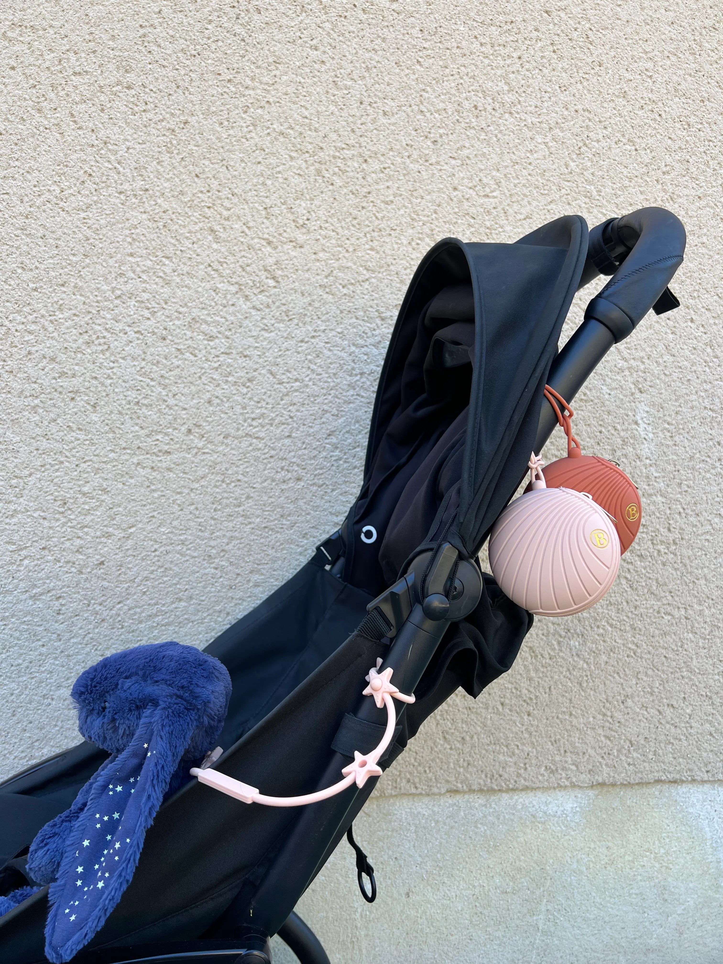 Boite a tetines en silicone rose attachee a une poussette avec un attache doudou pour poussette Lovie Link star rose.