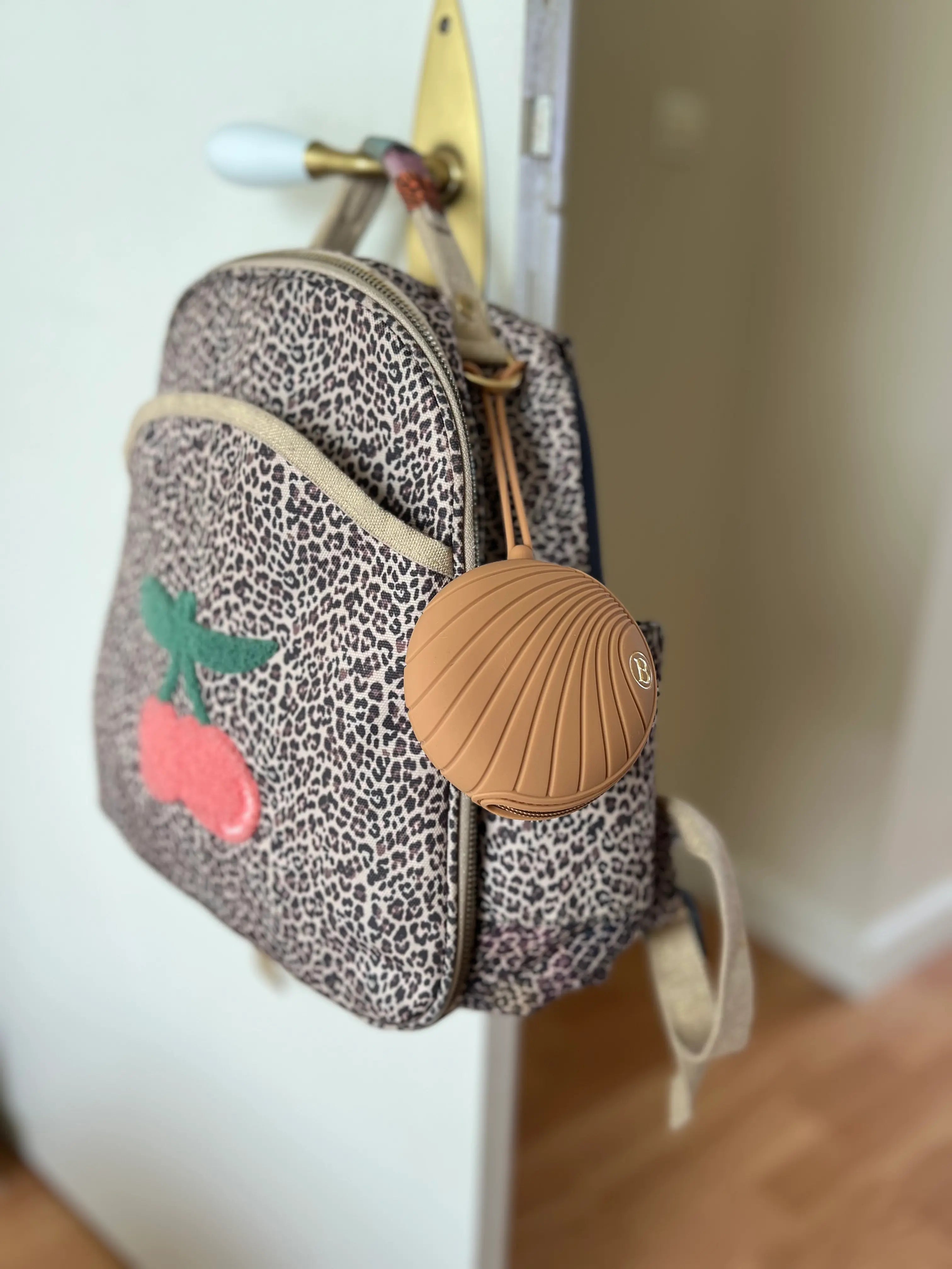 Boîte à Tétines en silicone Bim Bam Bloom attachée à un sac à dos léopard.