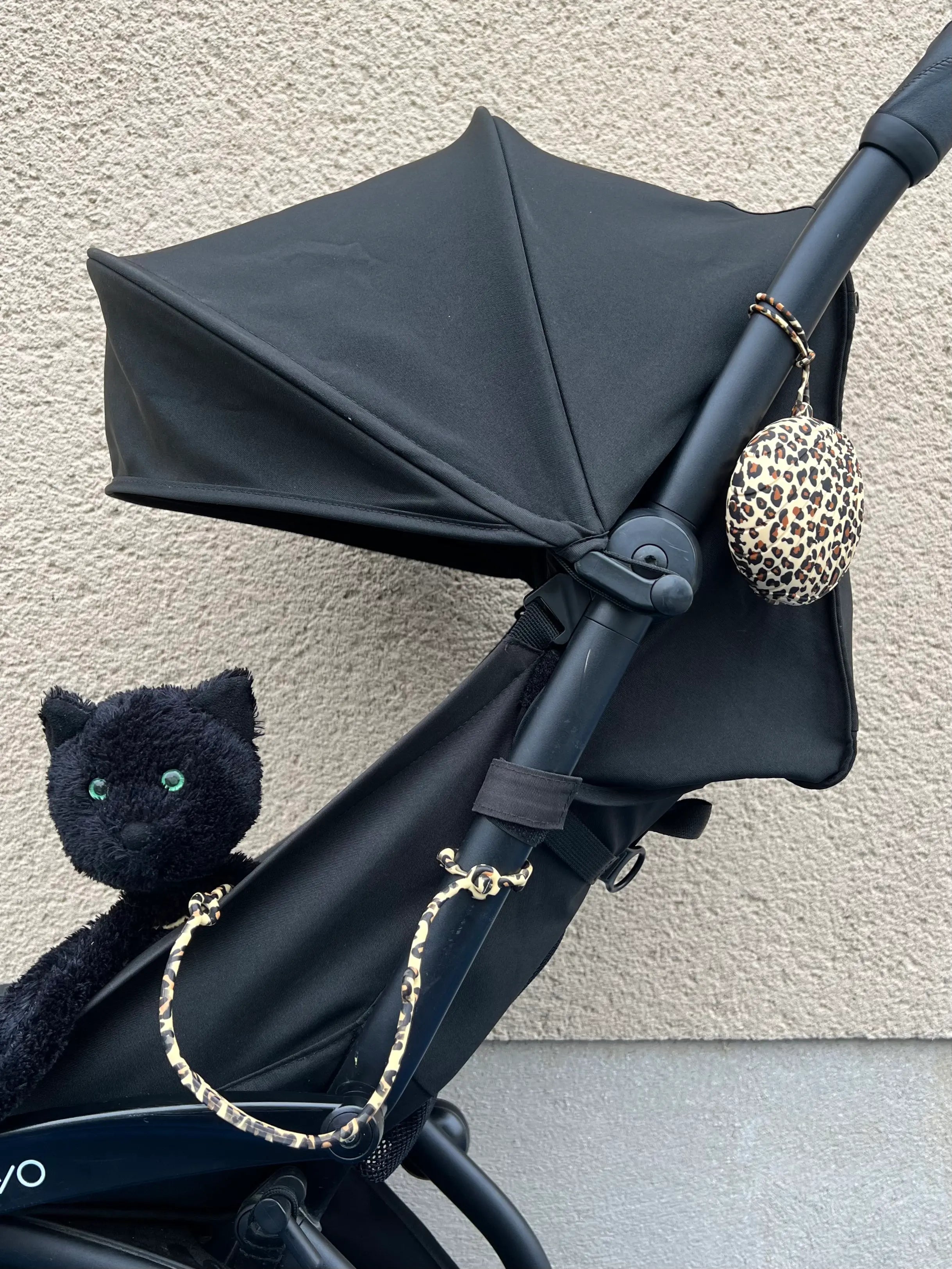 Boîte à tétine léopard Bim Bam Bloom avec un attache-doudou pour poussette léopard Lovie Link, attachée à la poussette.