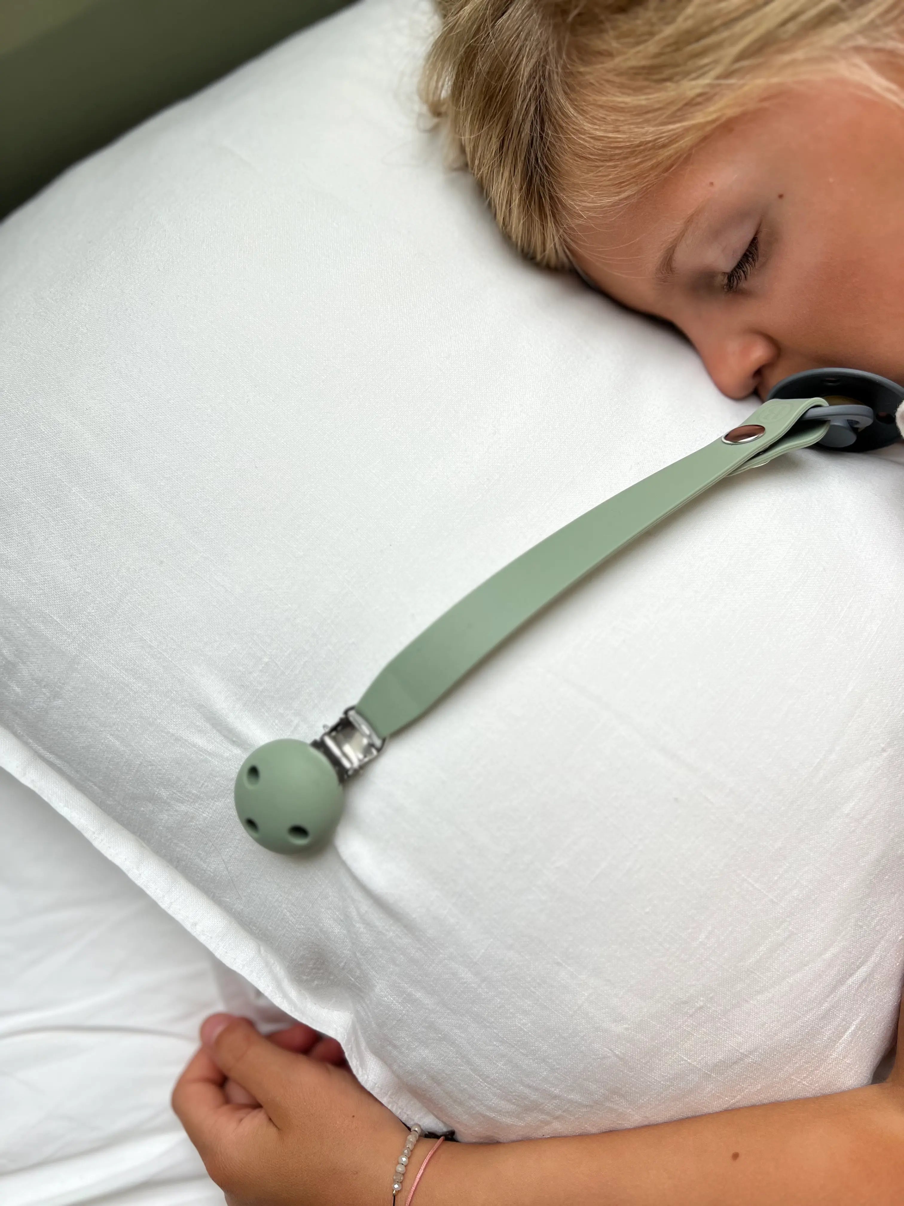 Petite fille portant l'attache-tétine Bim Bam Bloom en vert, gardant sa tétine à portée de main.