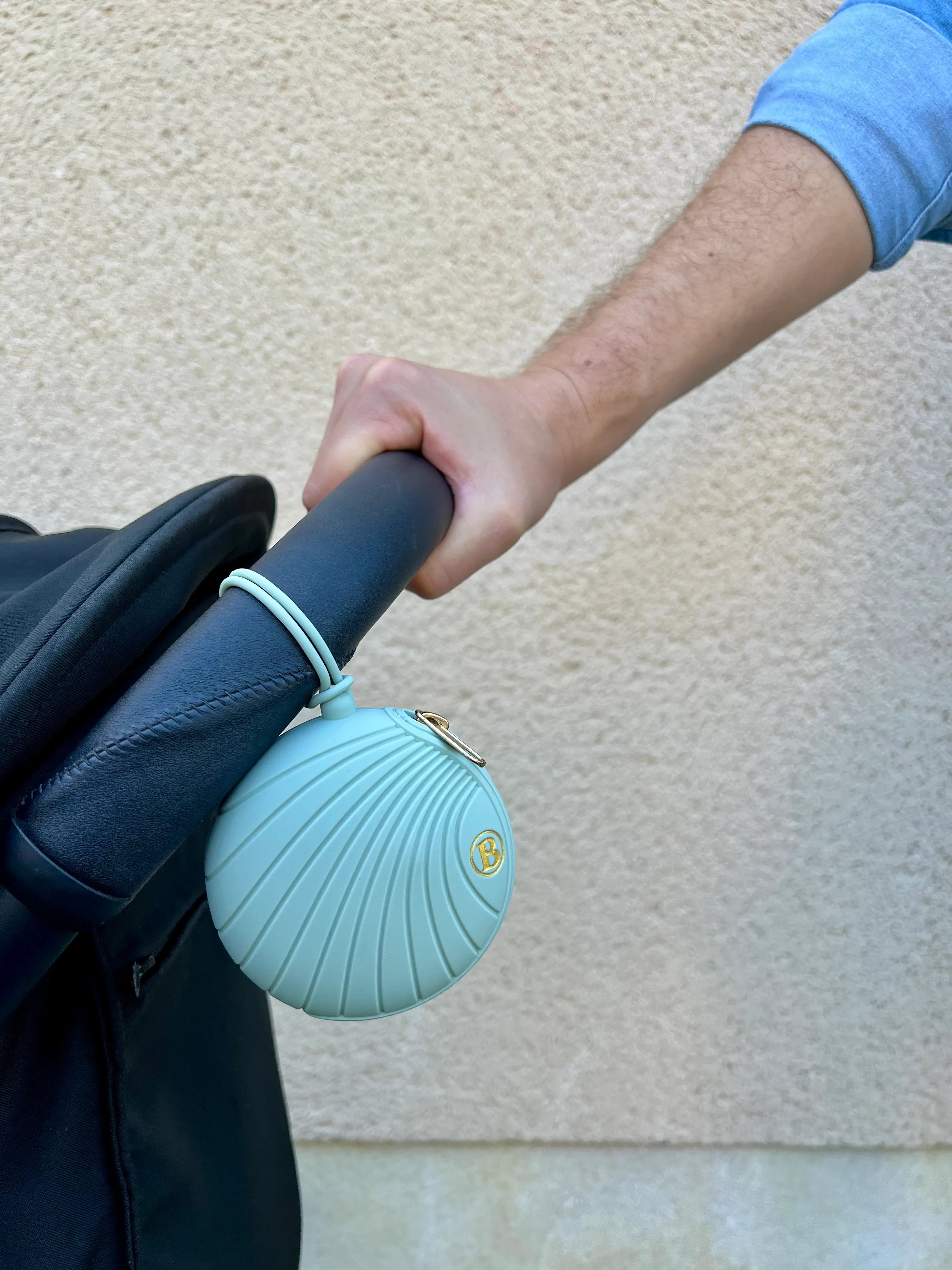 Gros plan sur la Boîte à tétine en silicone vert au design coquillage par Bim Bam Bloom. Attachée à une poussette,.