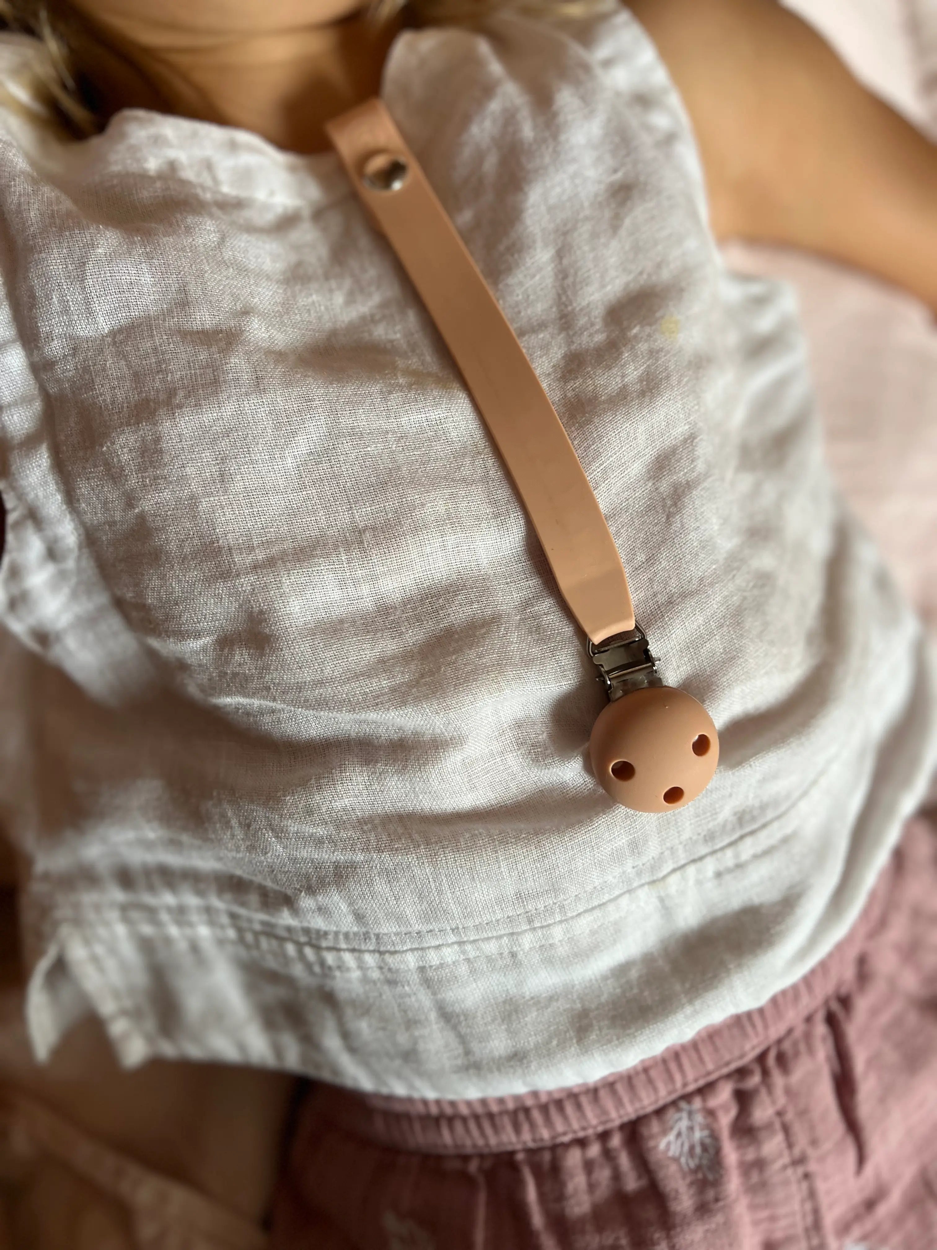 Attache-tétine pratique et adorable de Bim Bam Bloom en rose portée par une petite fille, permettant de garder la tétine de bébé toujours à portée de main et évitant les pertes lors des sorties.