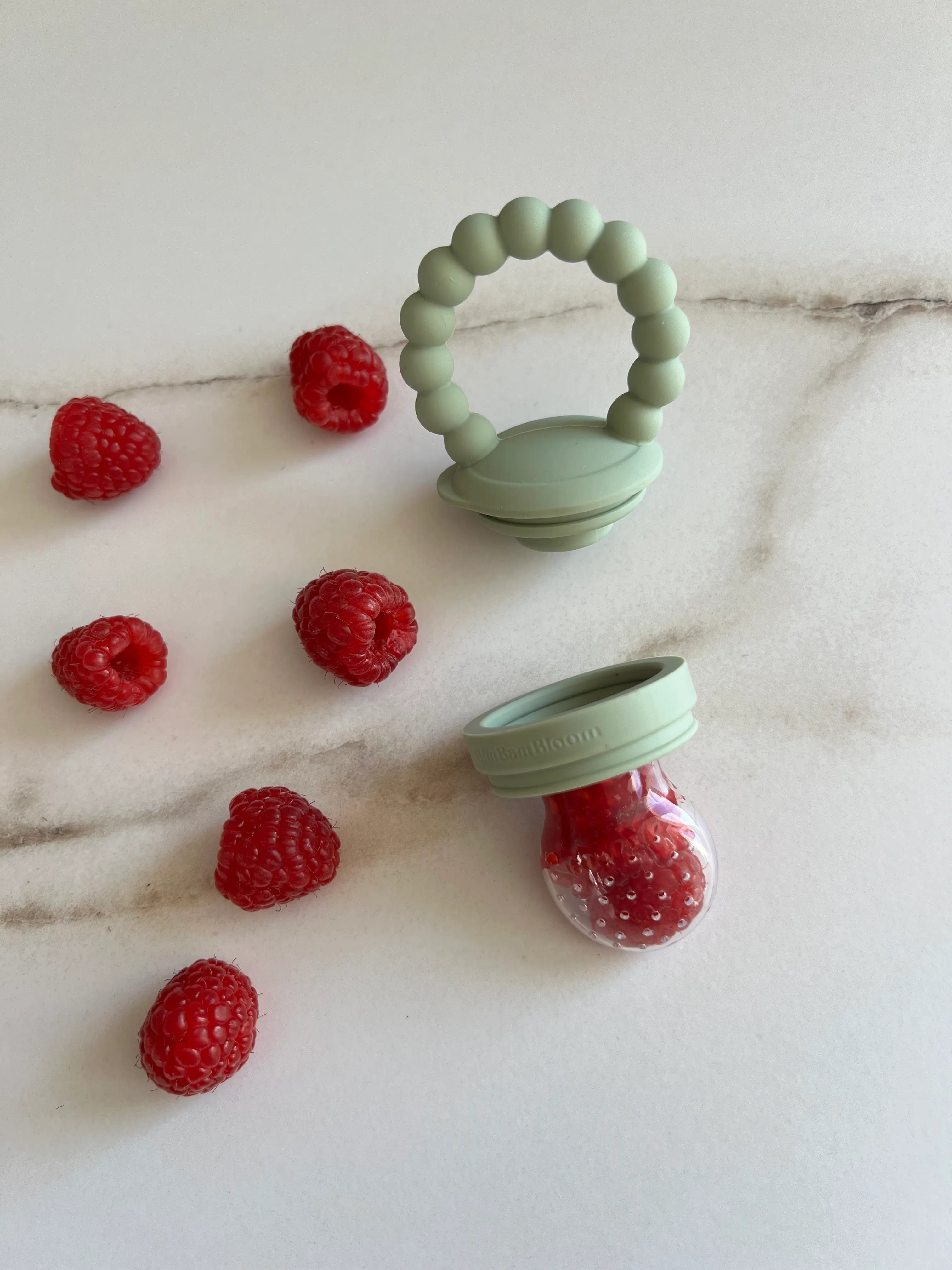 Tetine grignoteuse, a fruit, gourmande Yummy Tot vert en silicone Bim Bam Bloom remplie de framboises.