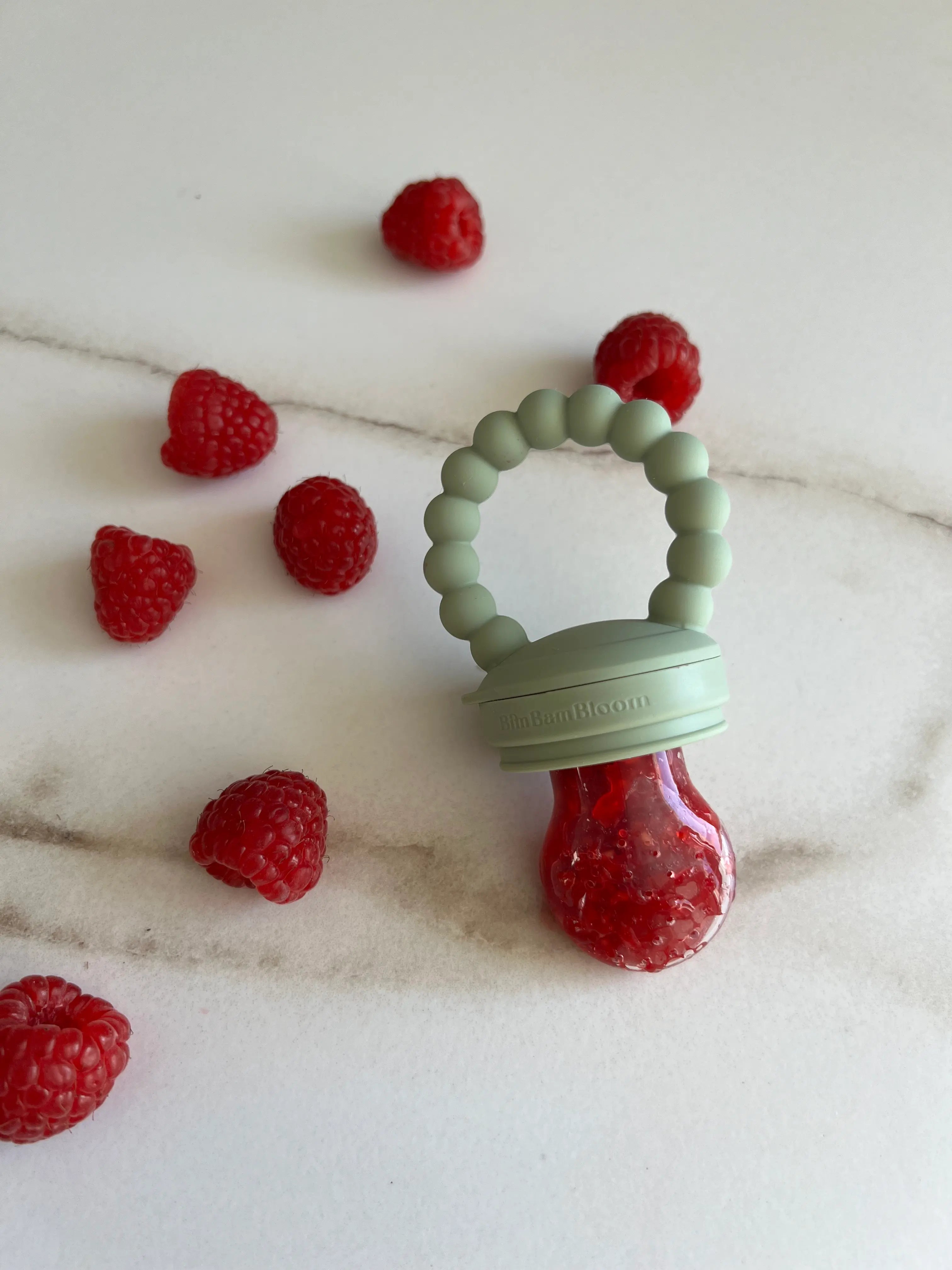 Tetine grignoteuse, a fruit, gourmande Yummy Tot vert en silicone Bim Bam Bloom remplie de framboises juteuse.