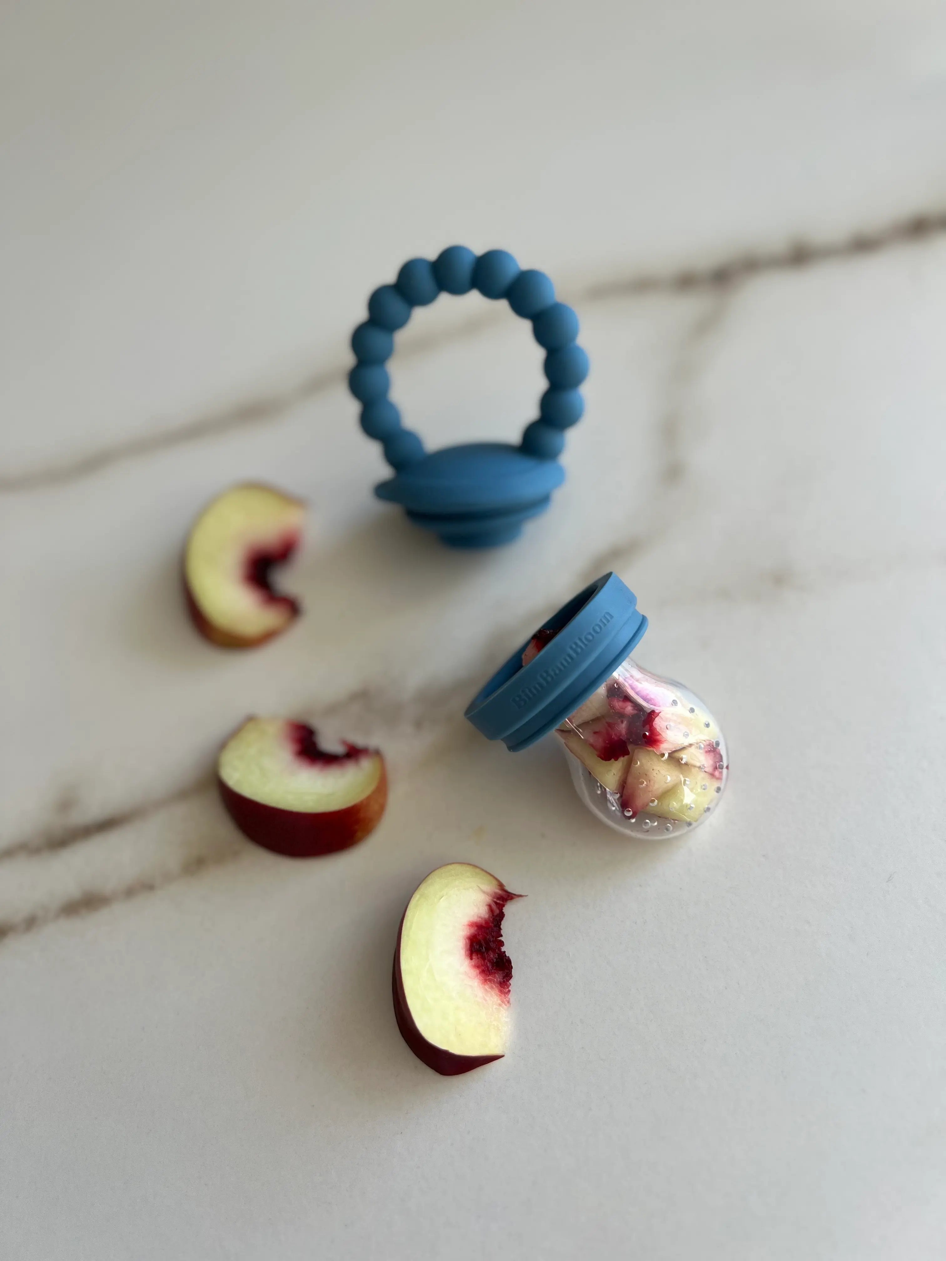 Tetine grignoteuse, gourmande, a fruit pour bebe en silicone Bleu Bim Bam Bloom remplie de morceaux de nectarines.