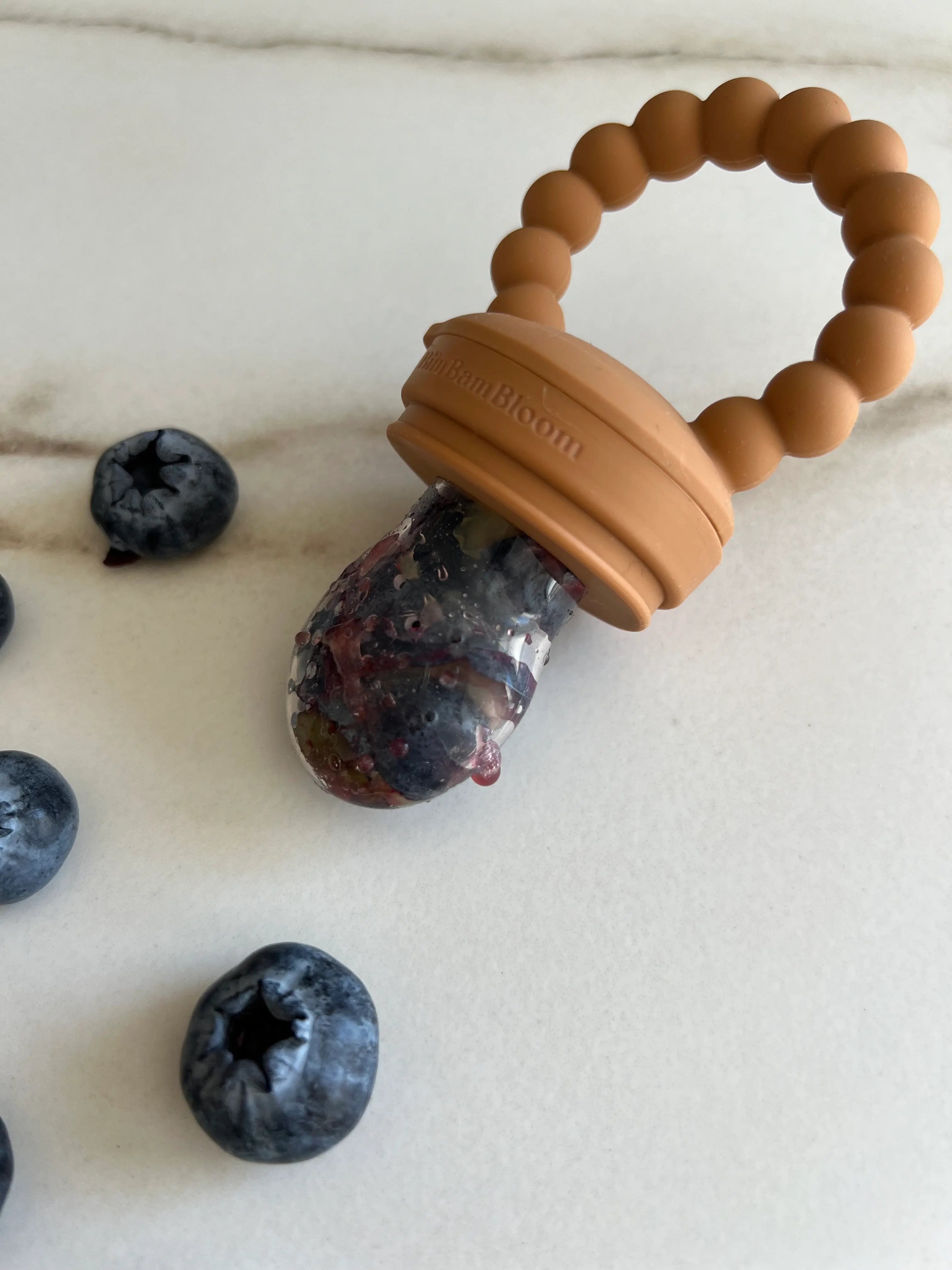 Gros plan sur la tetine grignoteuse en silicone camel Bim Bam Bloom remplie de myrtilles fraiches et juteuses.
