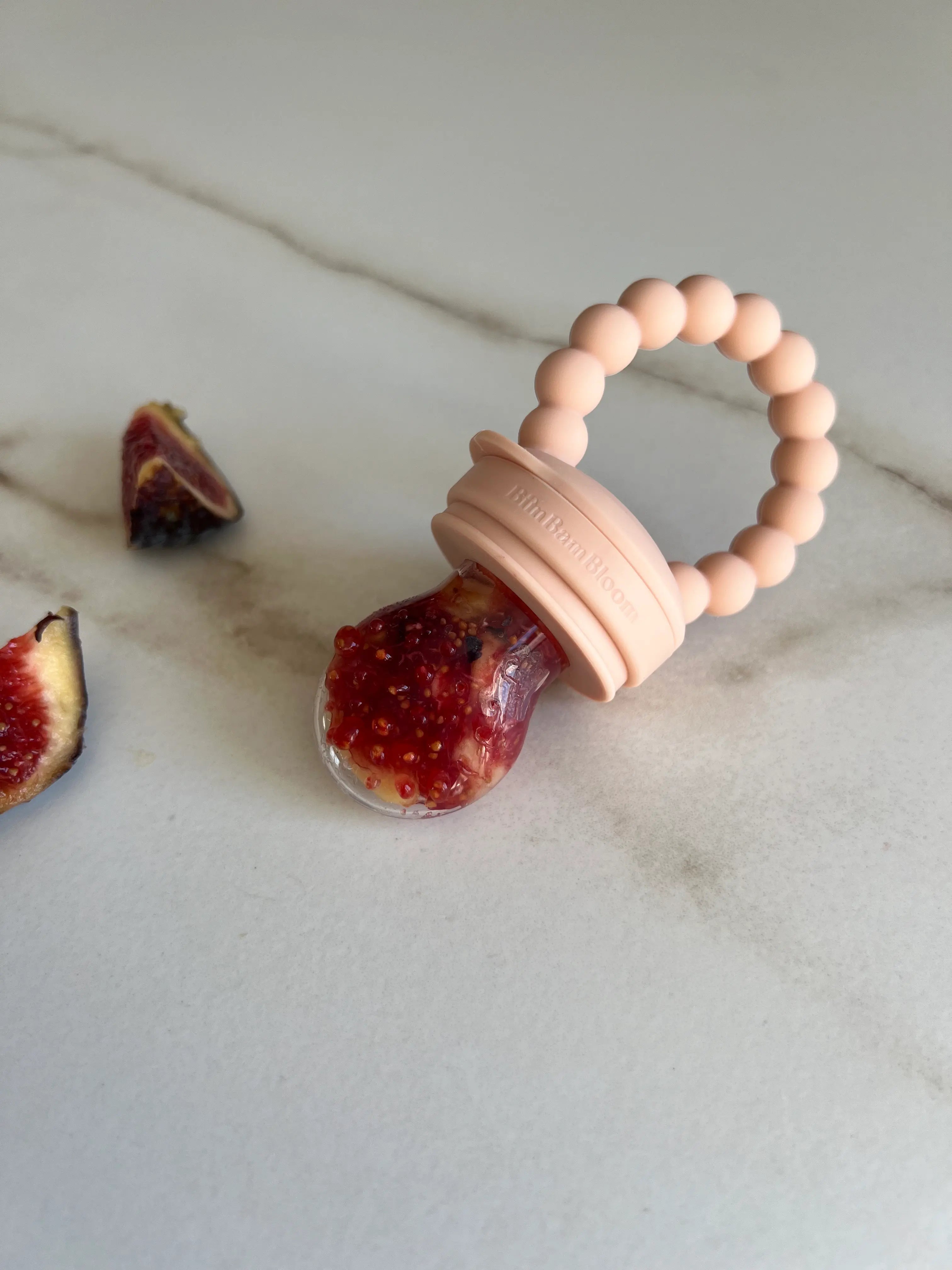 Cadeau de naissance original, pack tetine grignoteuse Yummy Tot Classic en silicone rose avec 3 tailles de tetines. Gros plan sur figue dans la tetine.